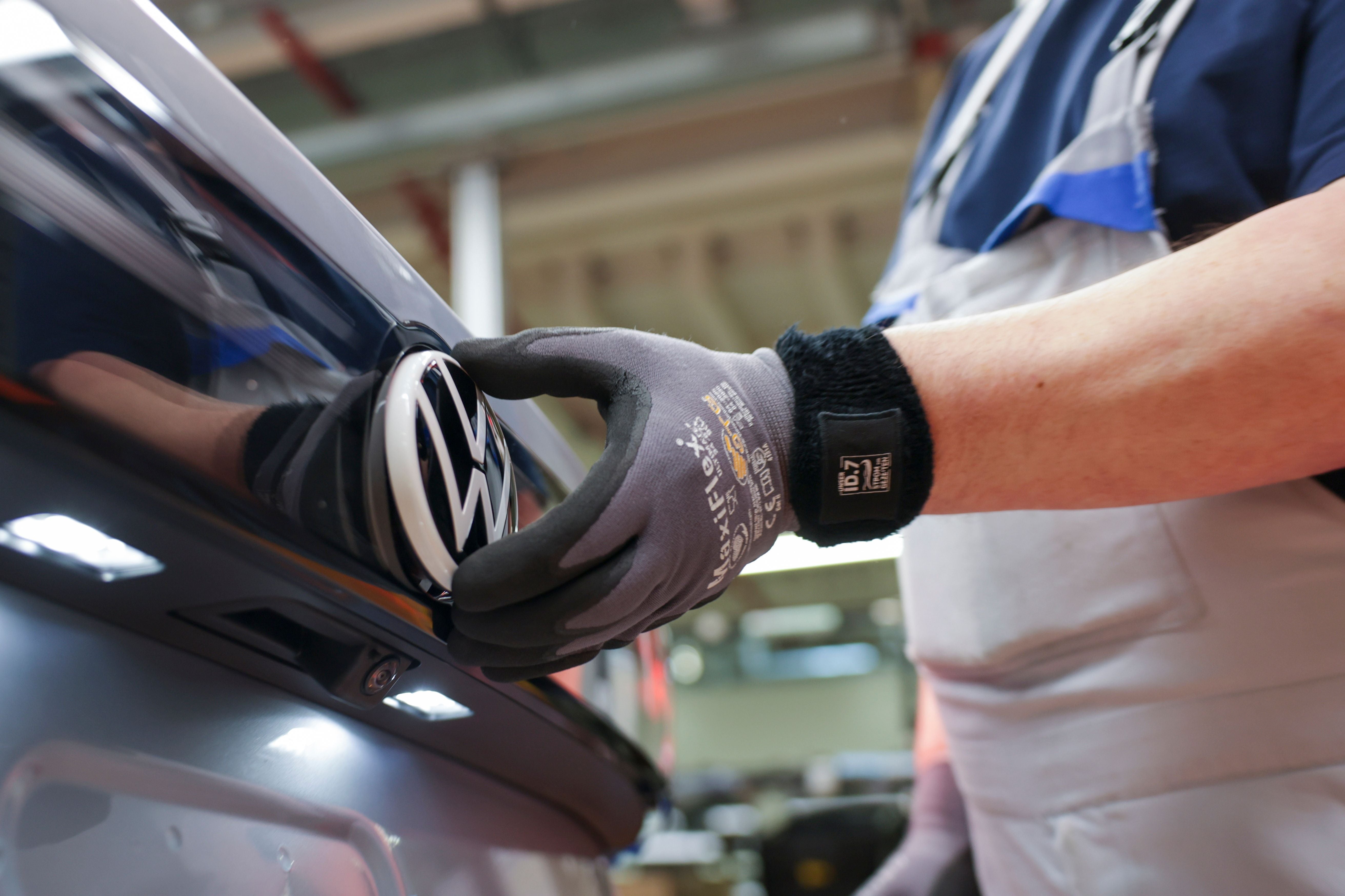Ein Mitarbeiter montiert das VW-Logo an einem Auto in einer Volkswagen-Fabrik.