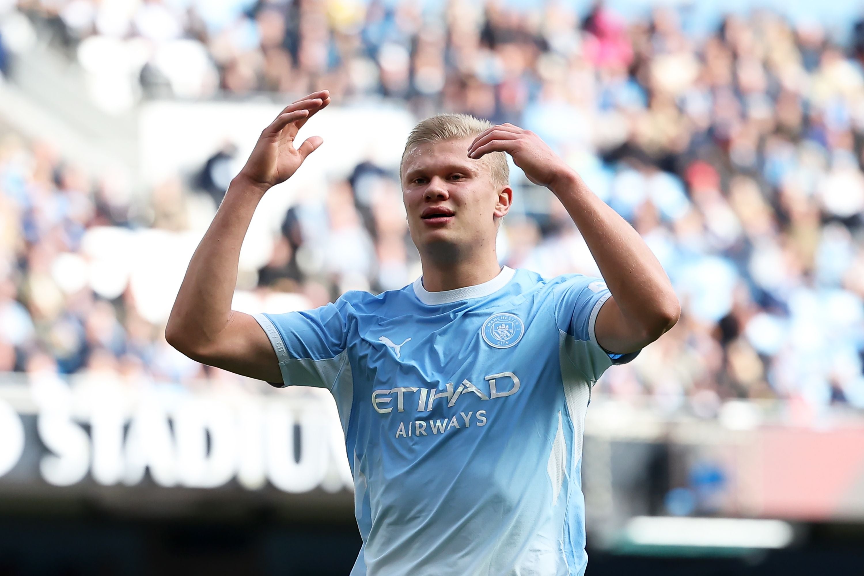 Fußballspieler im Manchester City-Trikot hebt die Arme nach einer verpassten Chance im Stadion.