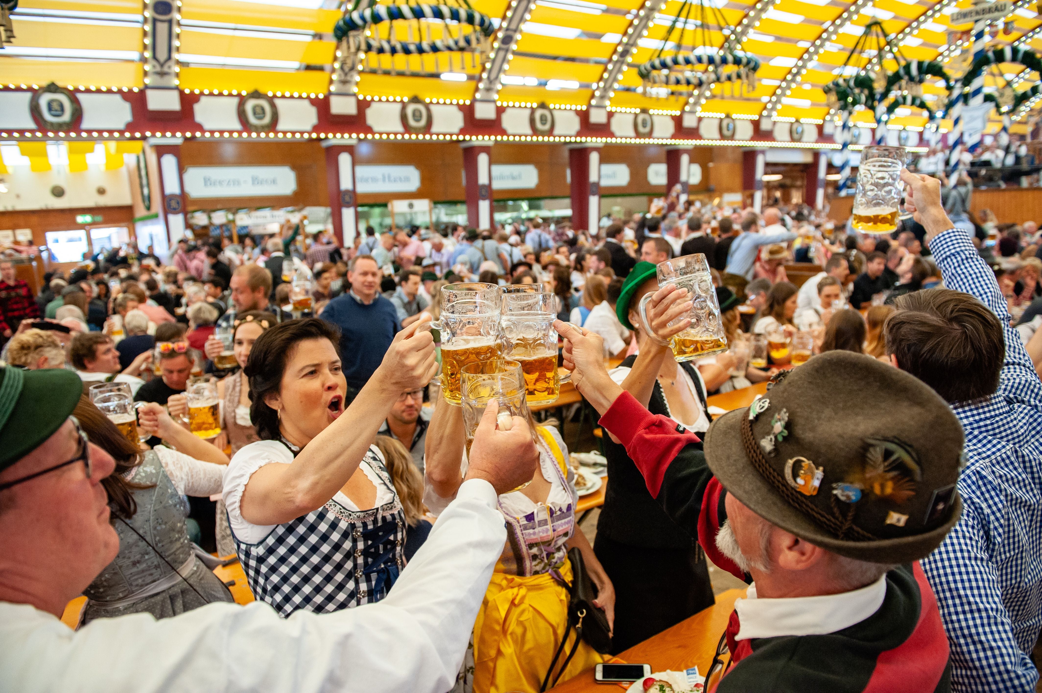 Menschen in Tracht stoßen in einem vollen Bierzelt auf dem Oktoberfest mit Bierkrügen an.