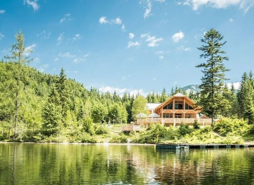 Holzhütte am Ufer des Ödensees, umgeben von Wald und blauem Himmel.