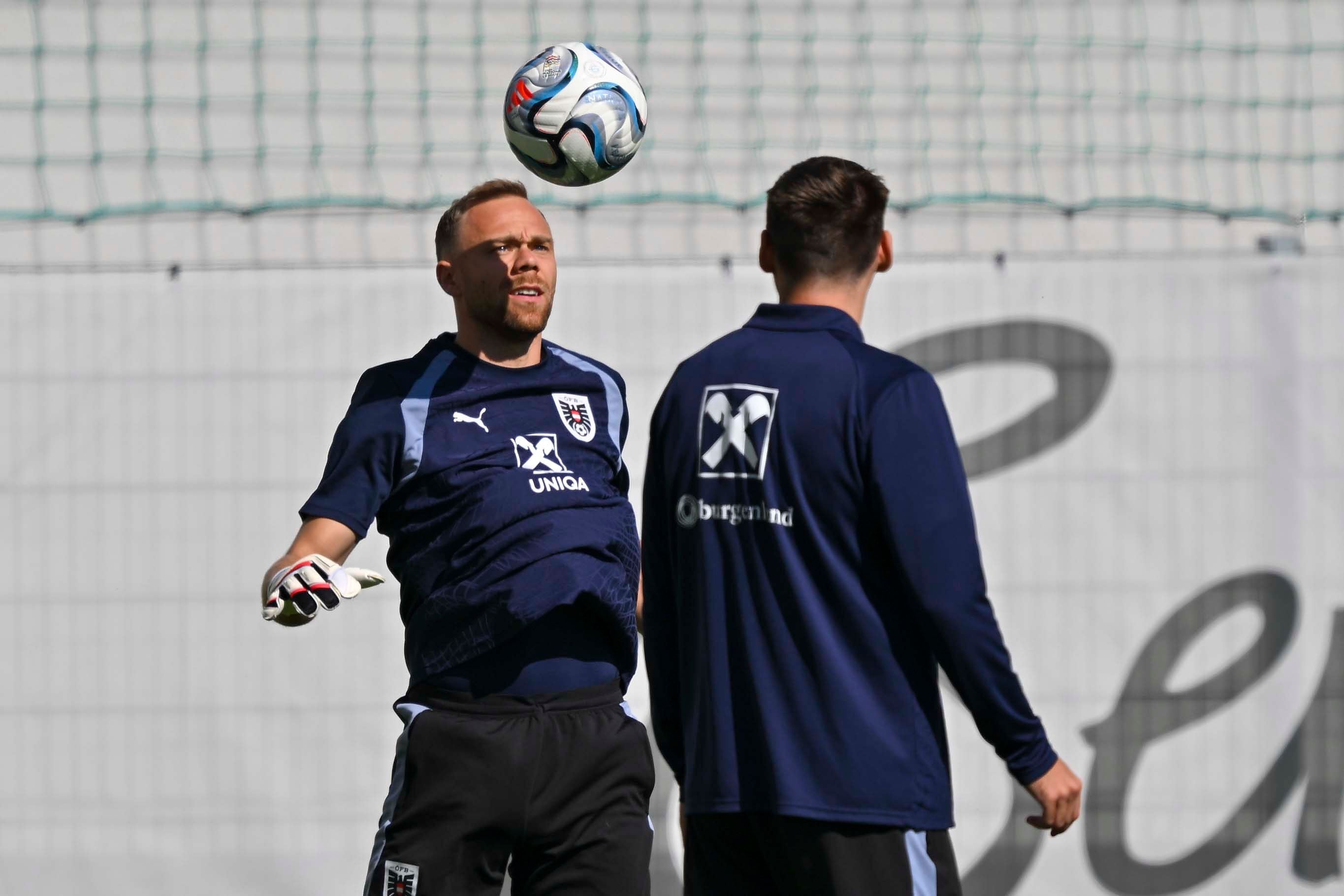 Zwei Fußballspieler beim Training, einer köpft einen Ball, beide tragen Österreich-Trikots.