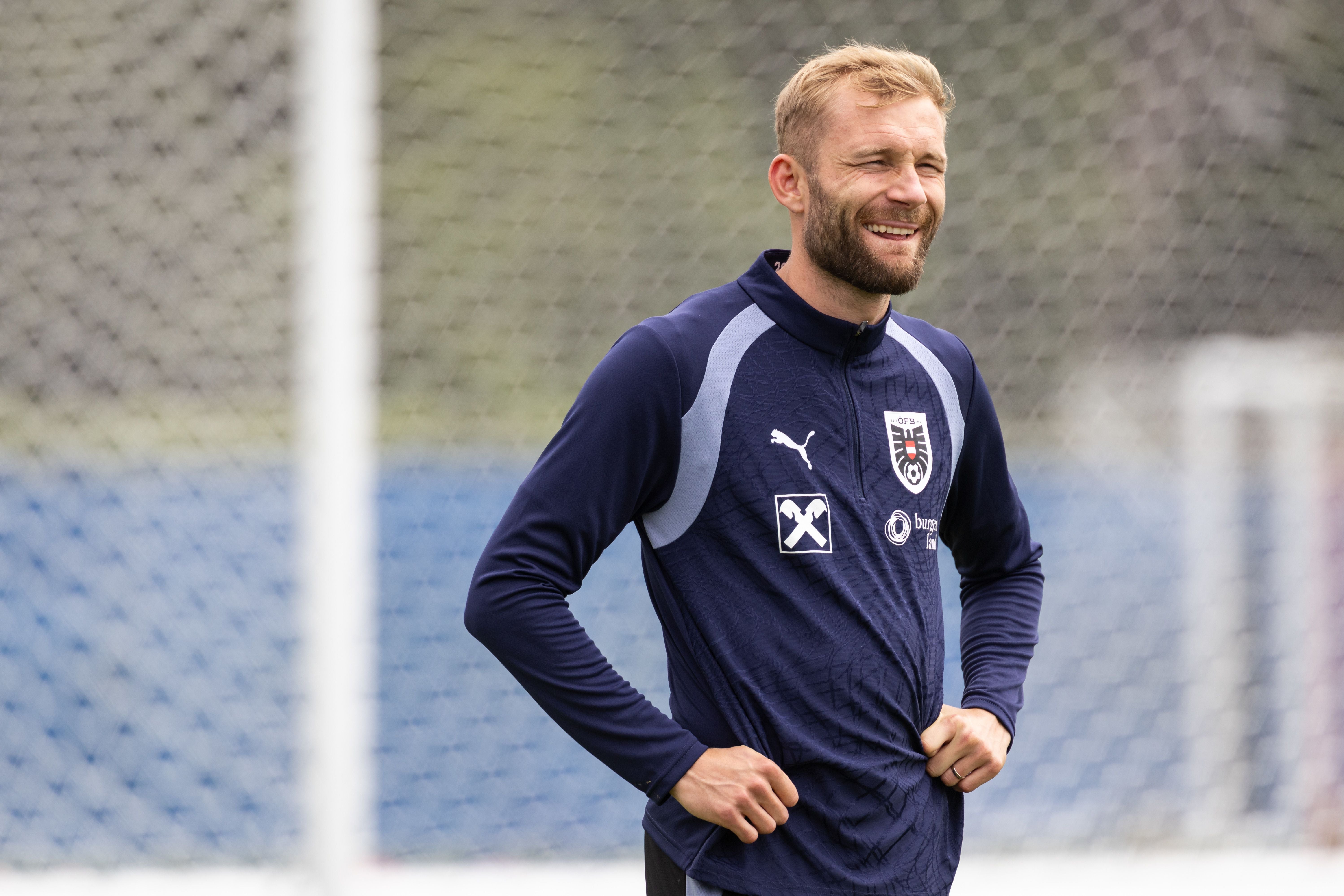 Ein Fußballspieler im Trainingsanzug lächelt während einer Trainingseinheit auf dem Spielfeld.