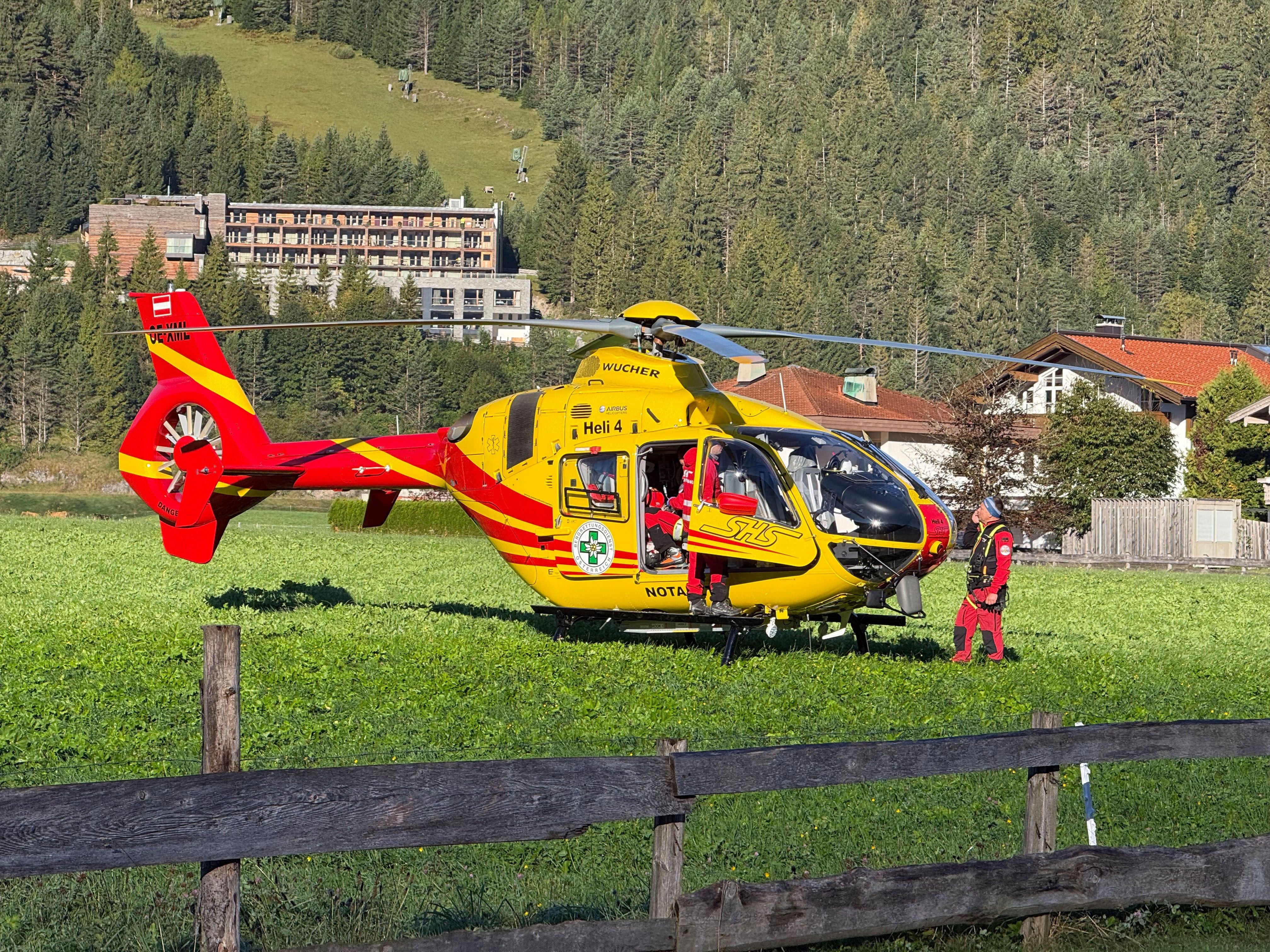 Ein gelber Rettungshubschrauber steht auf einer Wiese, daneben ein Notarzt in roter Kleidung.