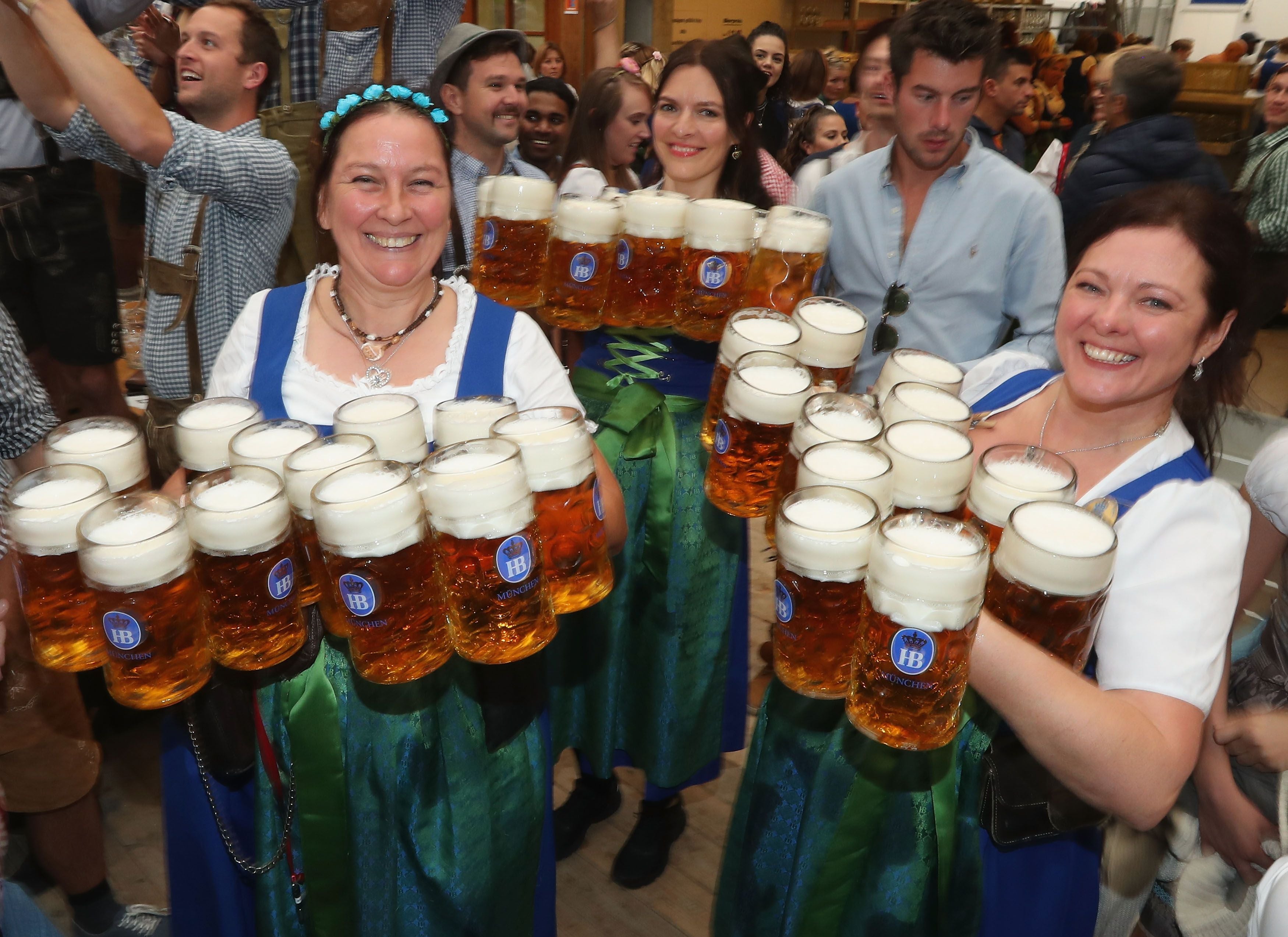 Drei Bedienungen im Dirndl tragen zahlreiche Bierkrüge auf dem Oktoberfest in München.