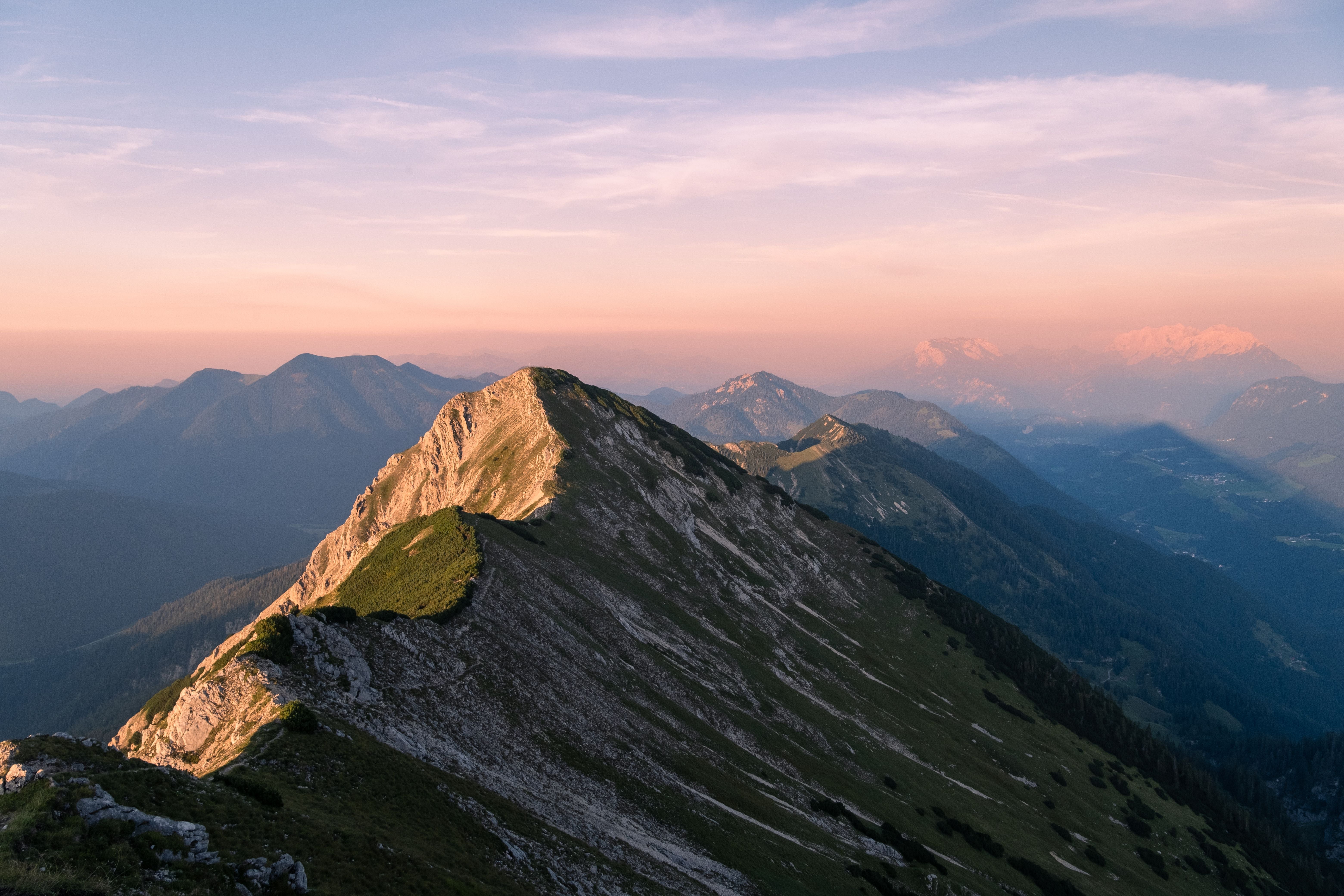 Bergkamm in Österreich bei Sonnenuntergang mit sanft beleuchteten Gipfeln und weitem Tal.