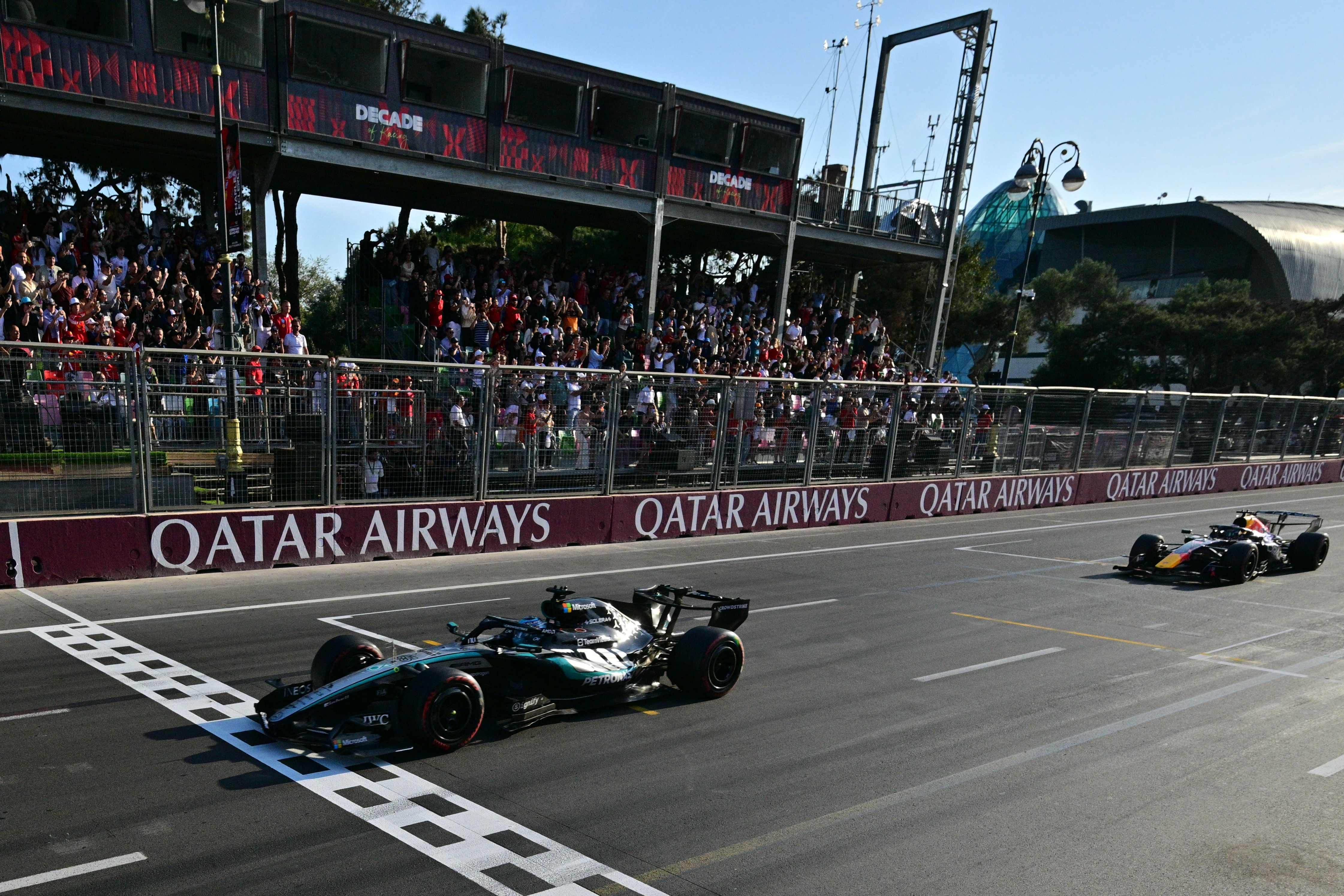 Ein Mercedes-Formel-1-Auto überquert vor einem Red Bull die Ziellinie, Zuschauer jubeln im Hintergrund.