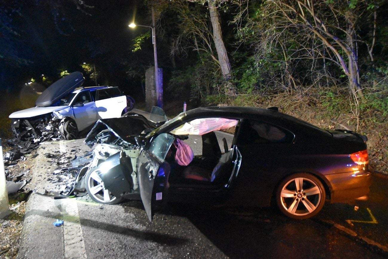 Zwei stark beschädigte Autos nach einem Unfall bei Nacht, Airbags ausgelöst, Umgebung bewaldet.
