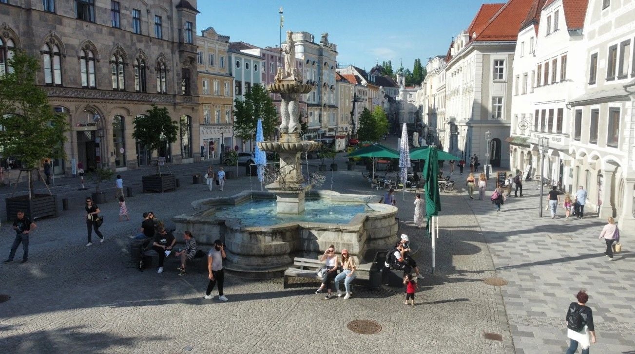 Brunnen auf einem belebten Platz in der Innenstadt von Steyr mit flanierenden Menschen.