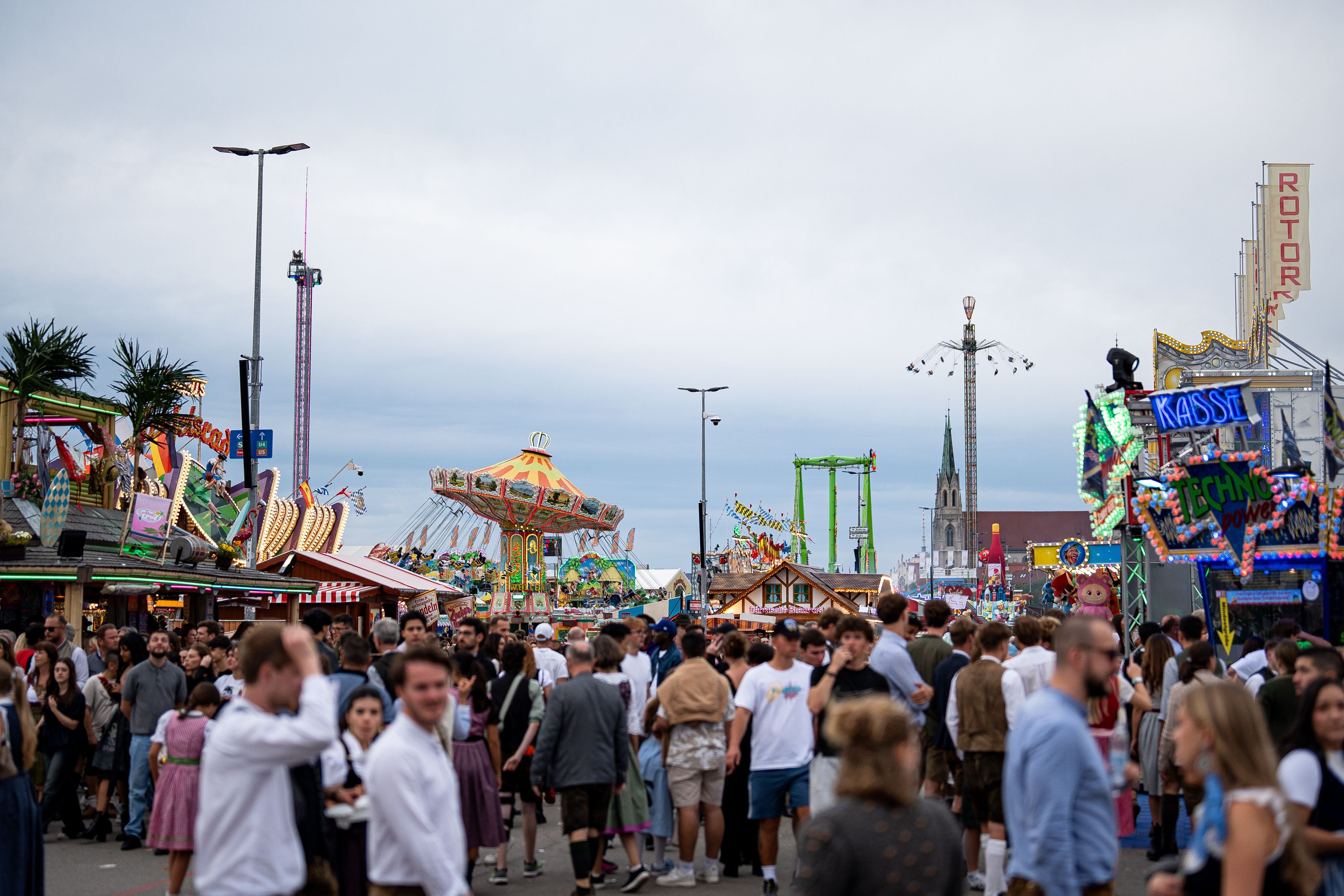 Menschenmengen auf dem Münchner Oktoberfest, mit Fahrgeschäften und bunten Lichtern im Hintergrund.