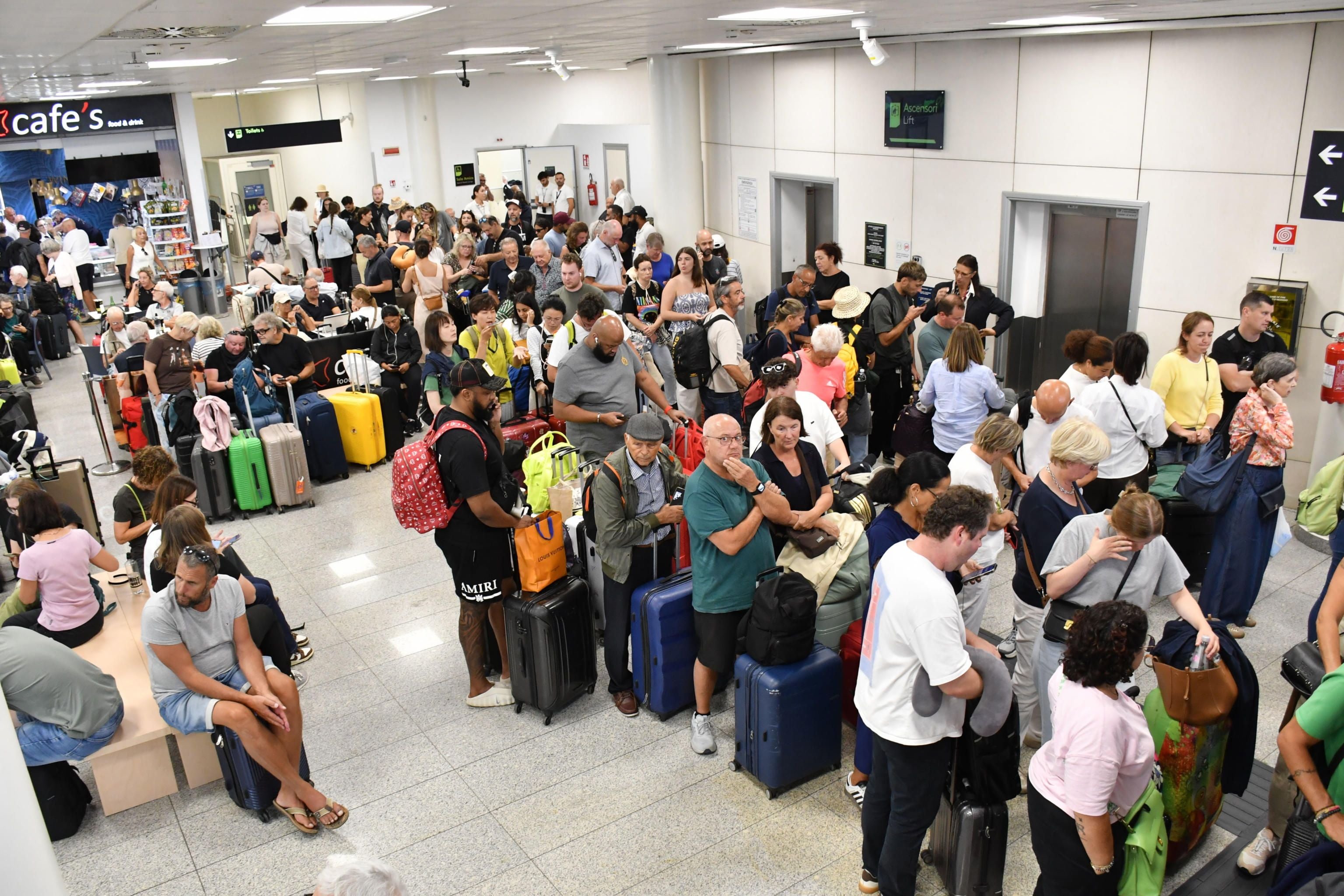 Viele Menschen mit Gepäck warten in einer vollen Abflughalle am Flughafen Catania.