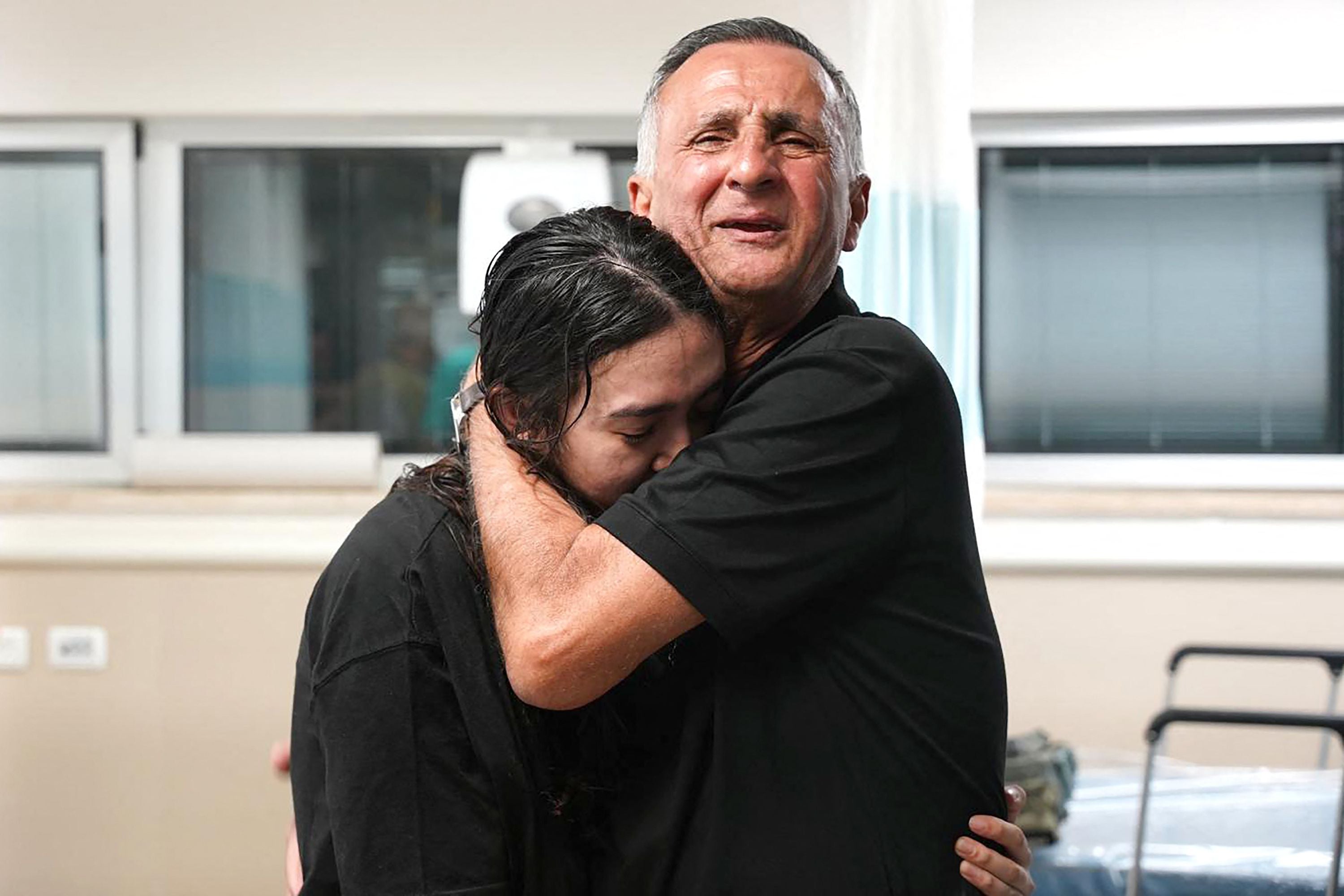 Eine junge Frau umarmt emotional einen älteren Mann in einem Krankenhauszimmer.