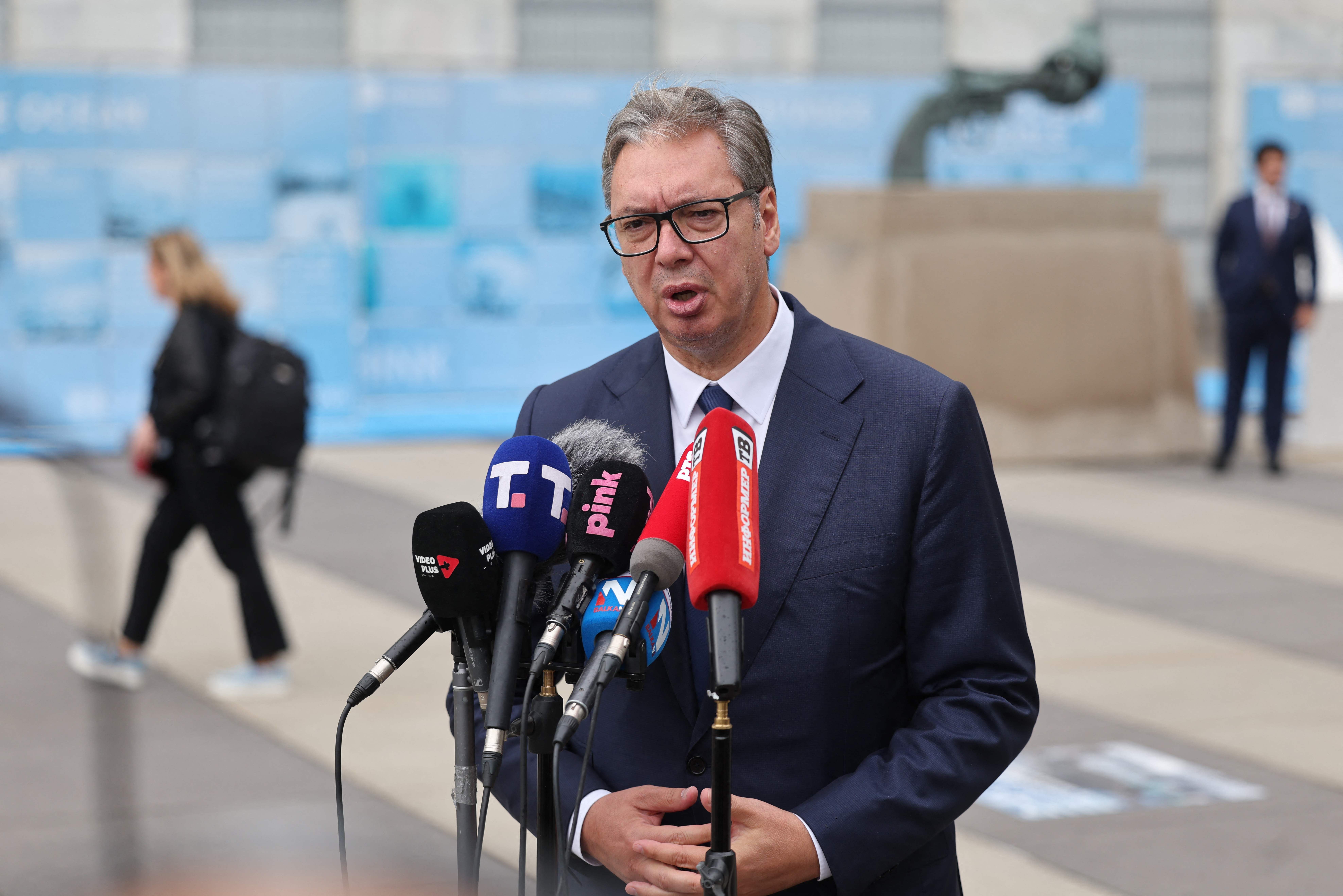 Ein Mann im Anzug spricht vor mehreren Mikrofonen bei einer Pressekonferenz im Freien.