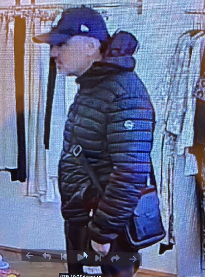 Mann mit dunkler Jacke und Mütze steht in einem Geschäft neben Kleiderständern.