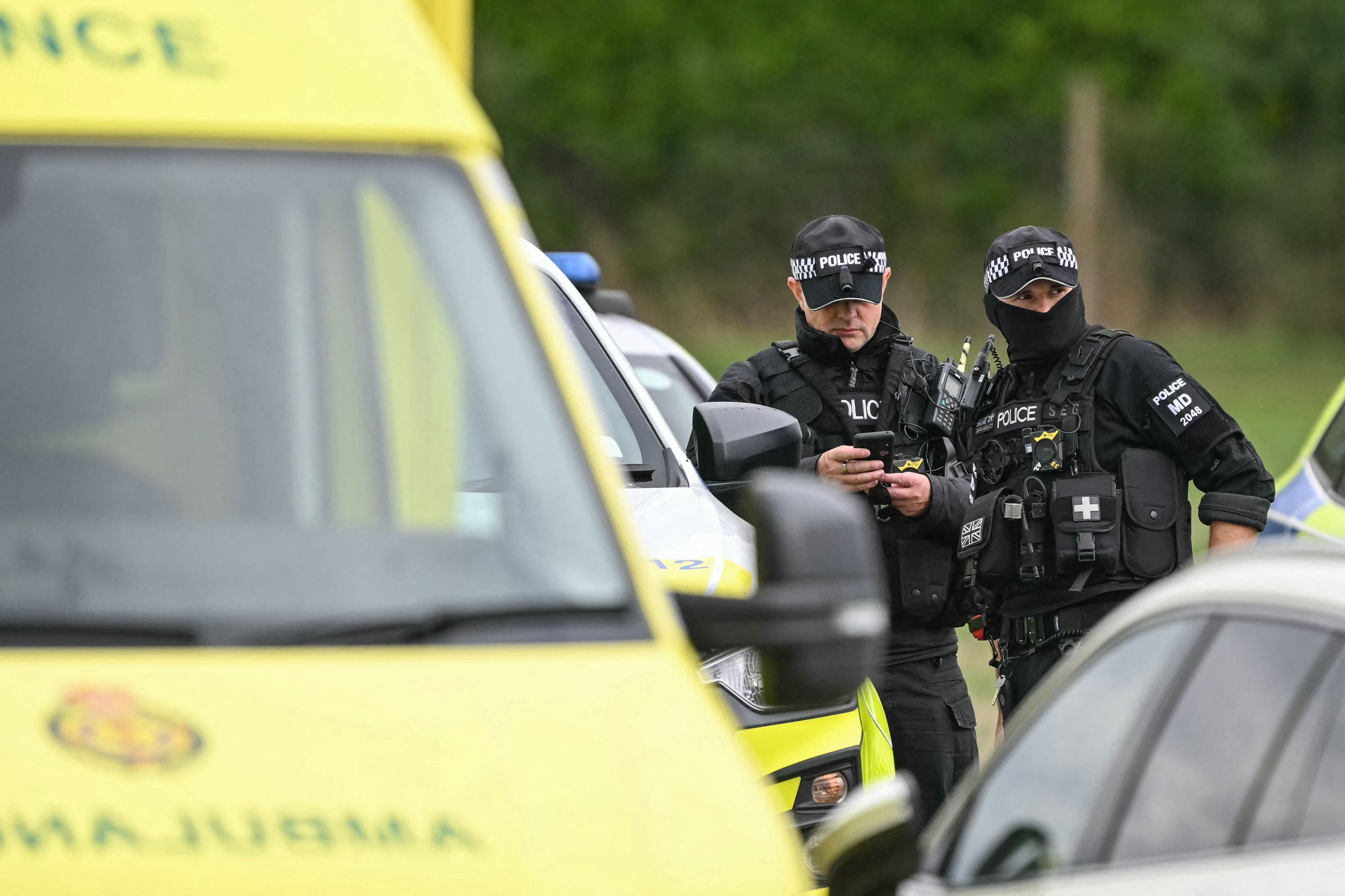Zwei britische Polizisten in Schutzausrüstung stehen neben Einsatzfahrzeugen und sprechen miteinander.