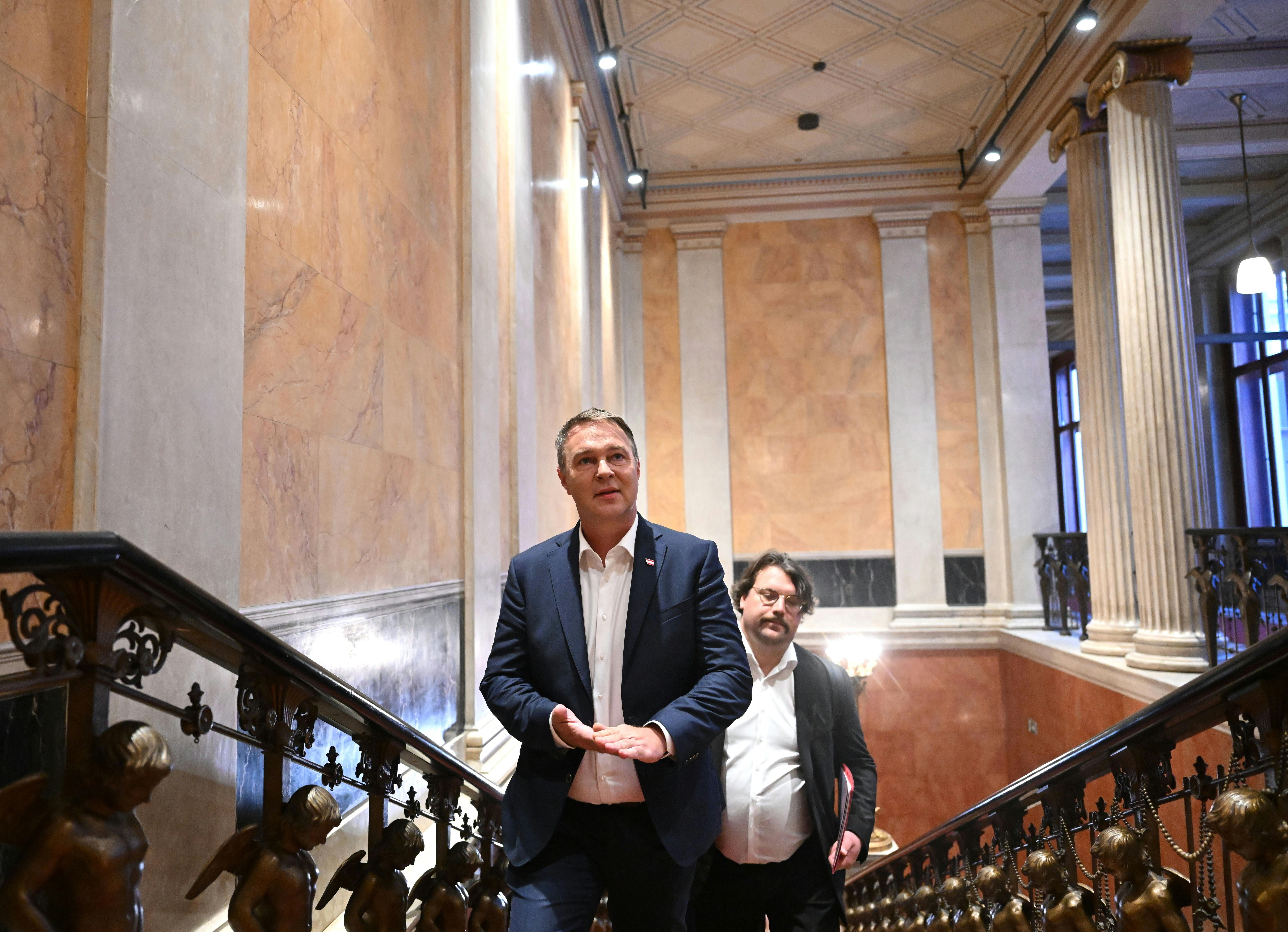 Zwei Männer im Anzug gehen eine prunkvolle Treppe im historischen Gebäude hinauf.
