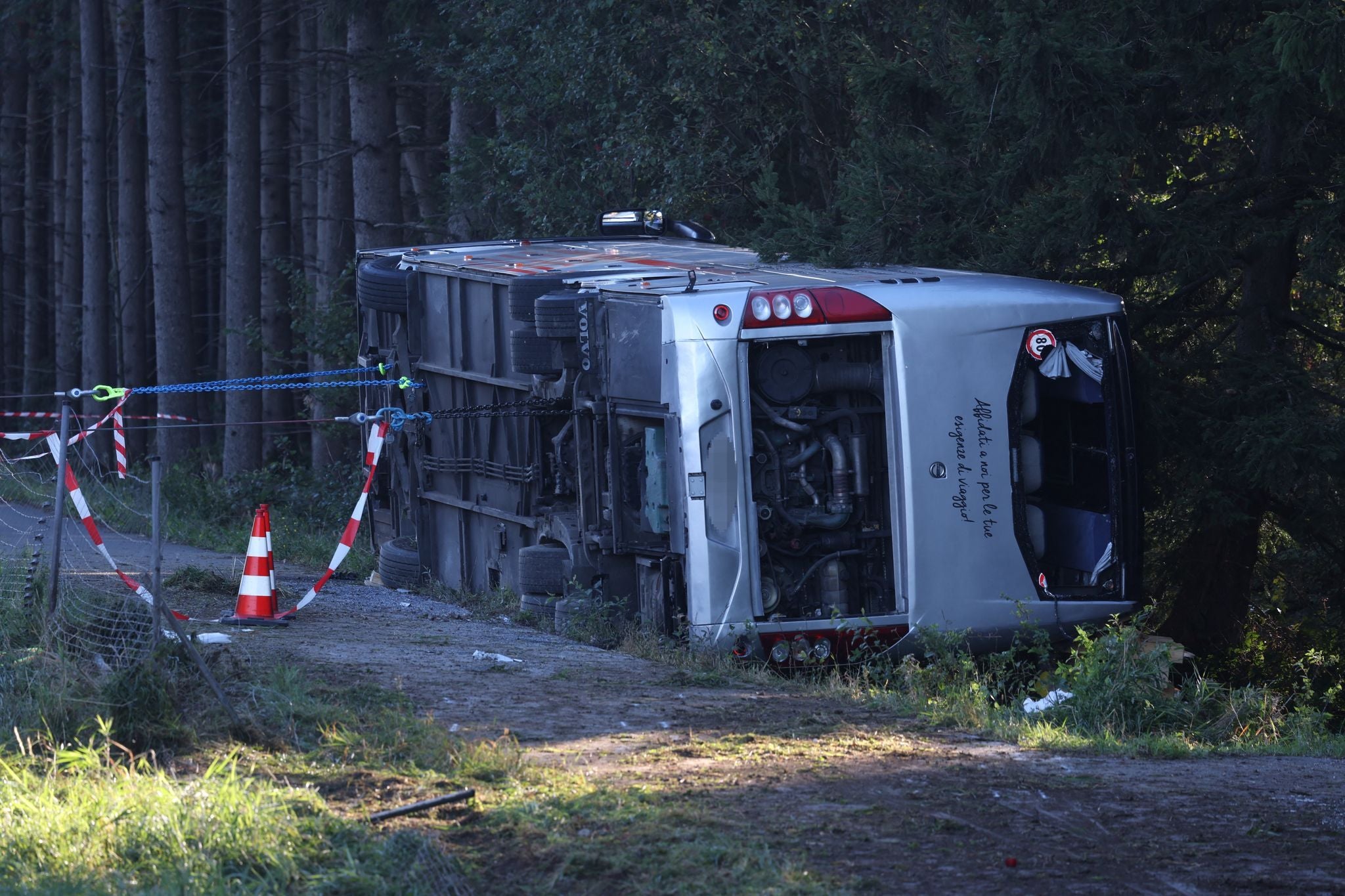 Ein Reisebus liegt umgekippt neben einer Straße, von Absperrband und Kegeln gesichert.
