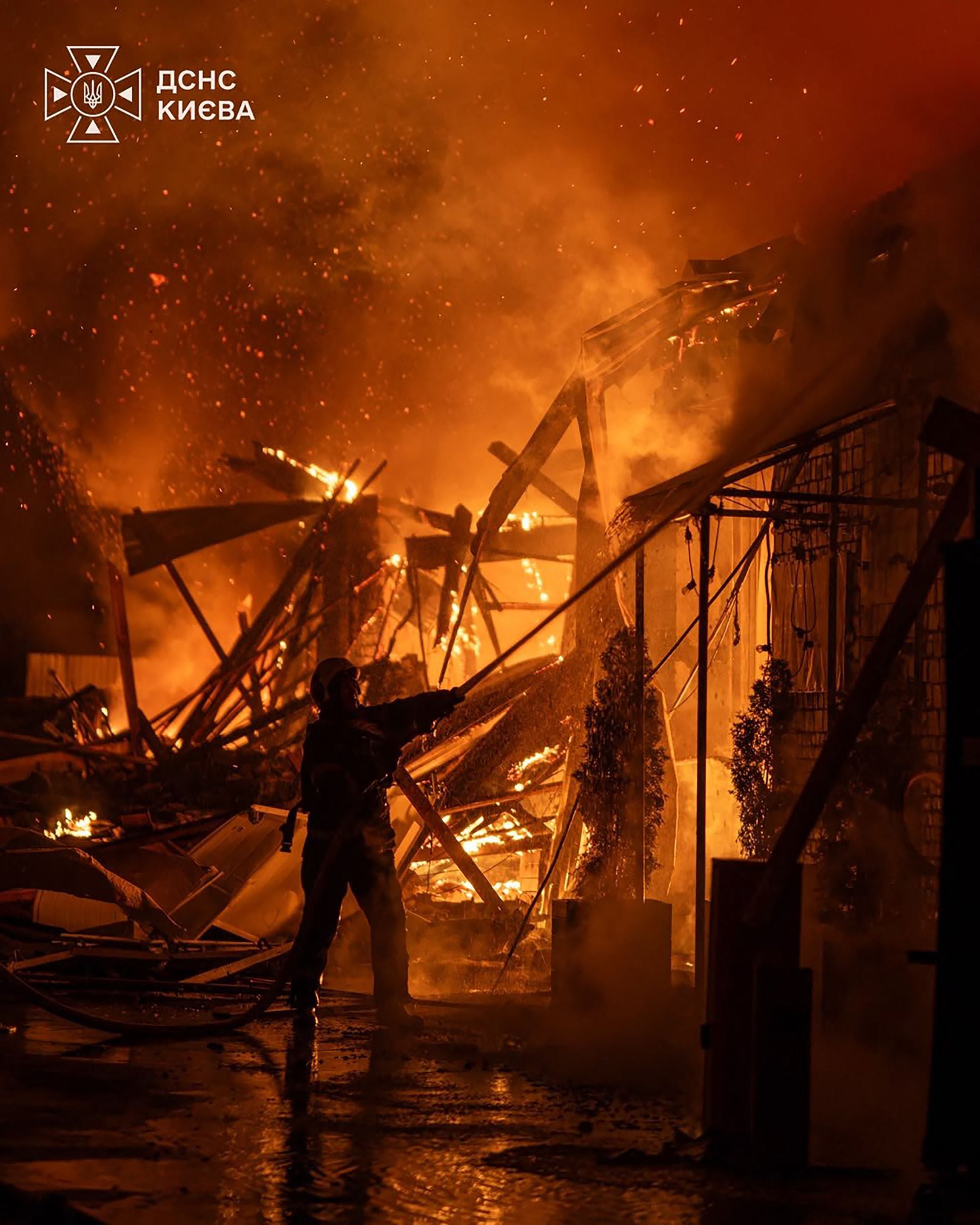Ein Feuerwehrmann löscht einen Großbrand an einer zerstörten Werkstatt bei Nacht in Kiew.