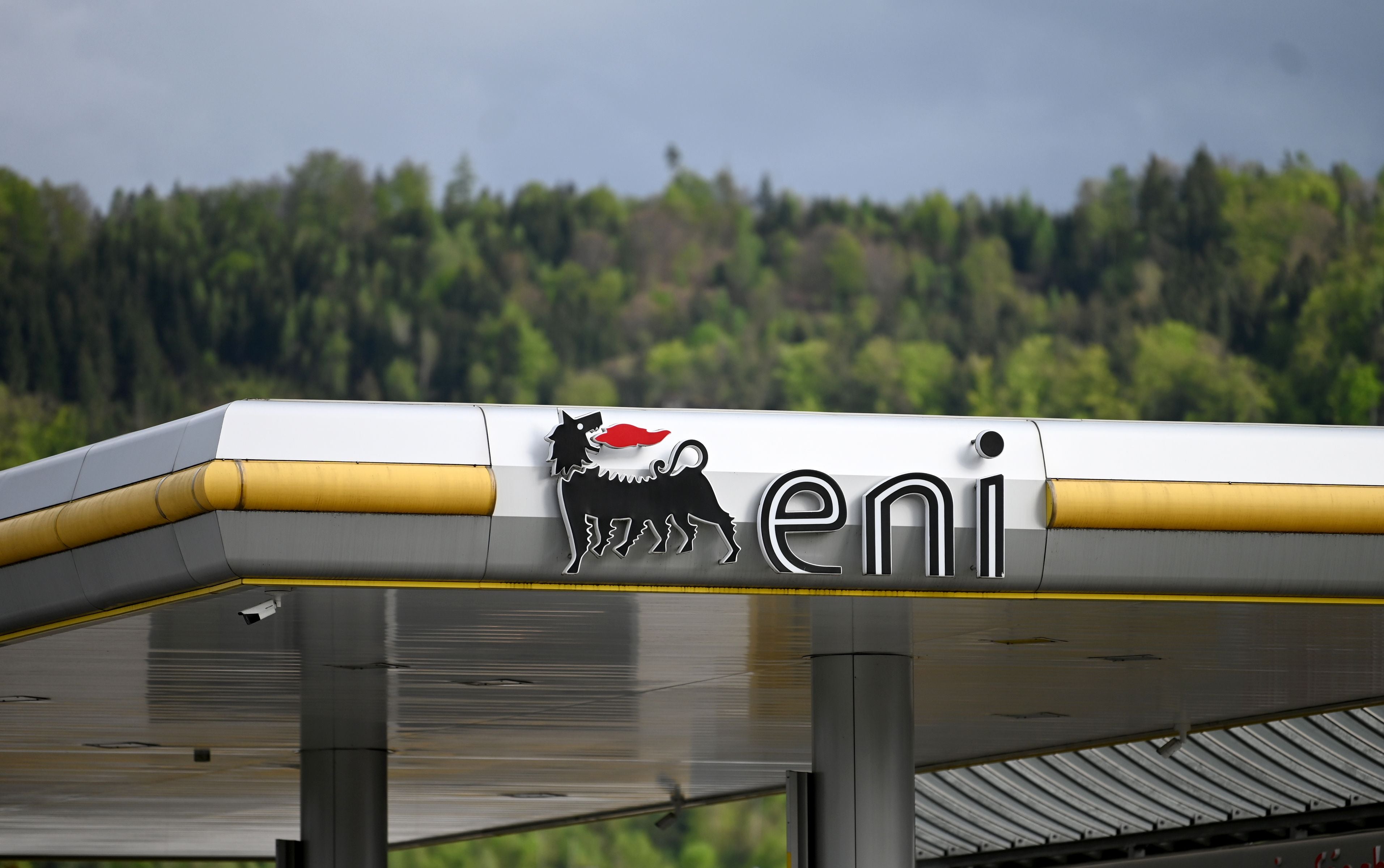 Das Logo einer Eni-Tankstelle mit gelbem Streifen vor bewaldetem Hintergrund.