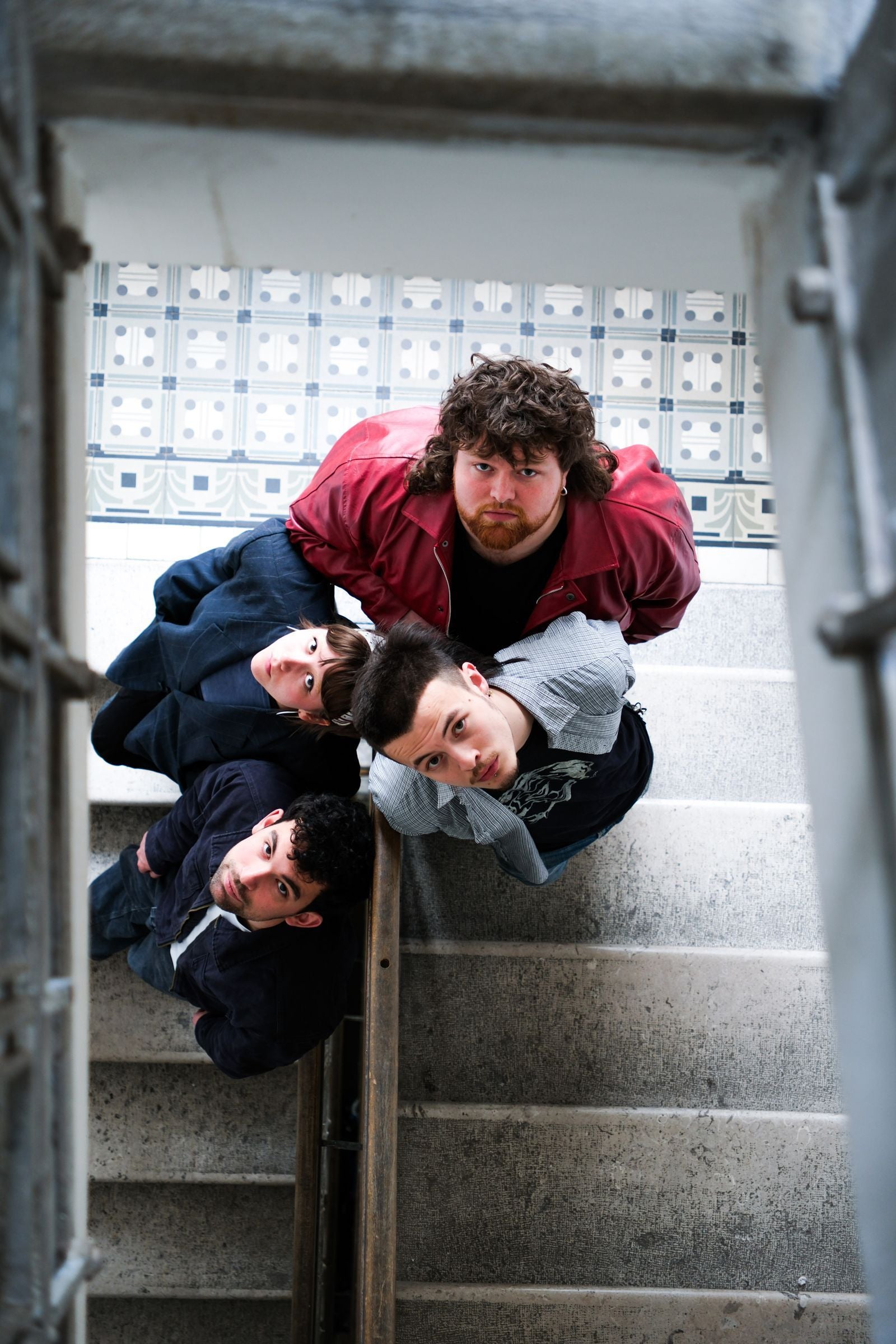 Vier junge Menschen stehen auf einer Treppe und blicken nach oben in die Kamera.