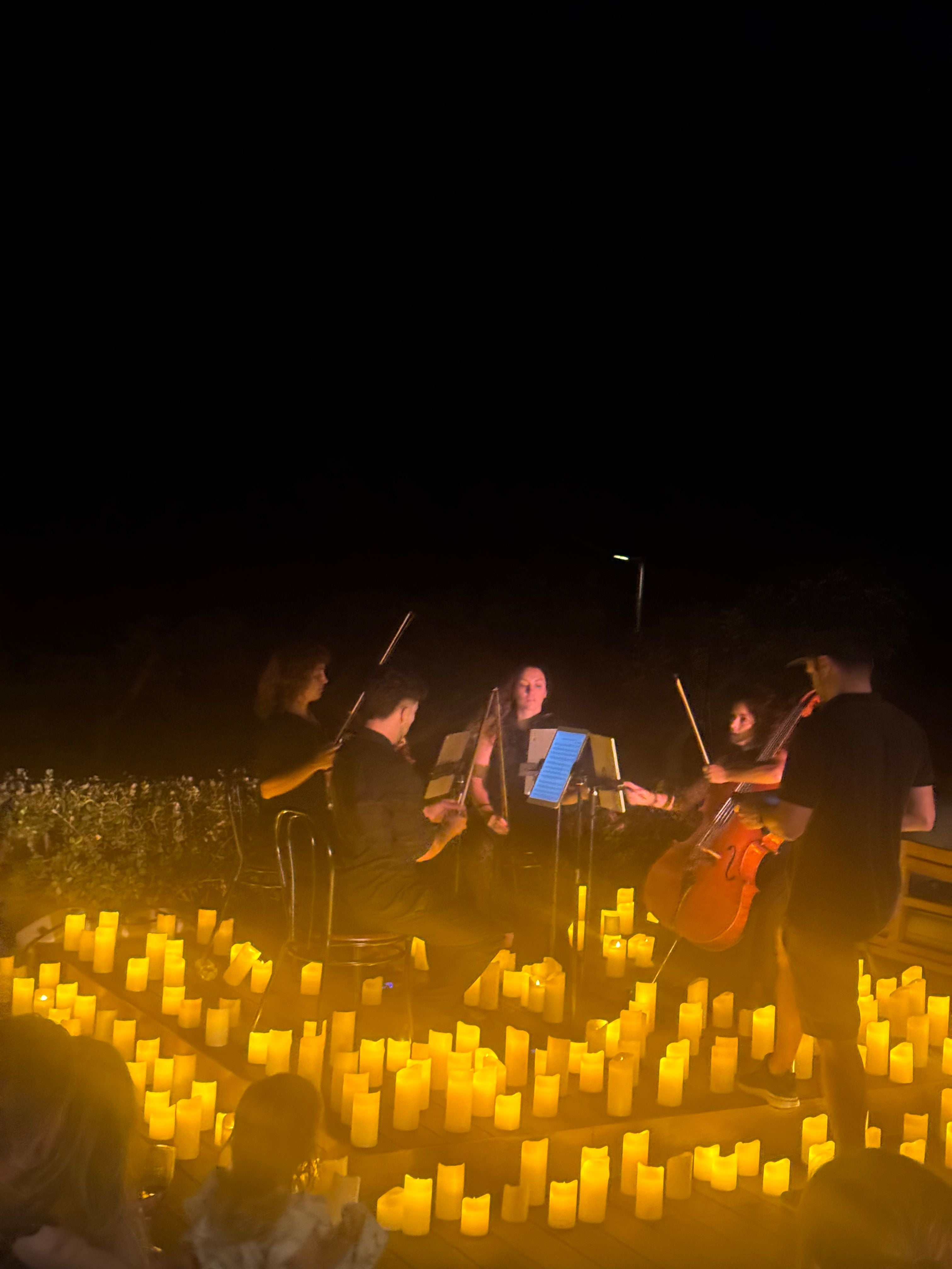 Streichquartett spielt nachts umgeben von vielen Kerzen im Freien im Ikos Andalusien.