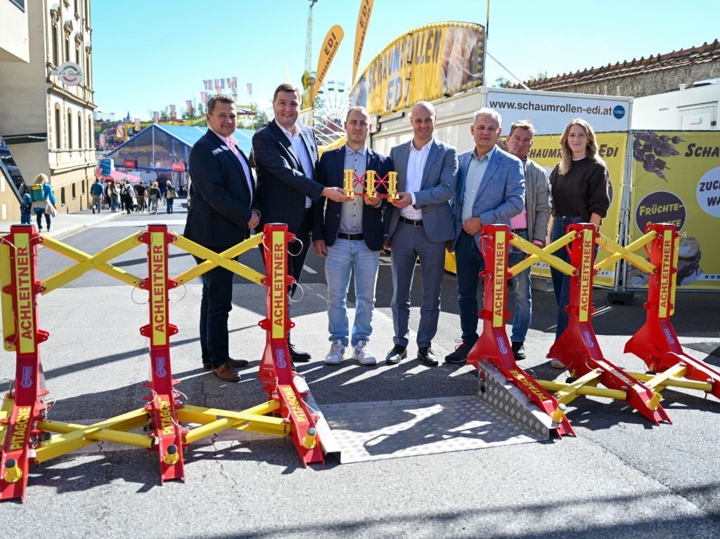 Sechs Personen stehen vor mobilen Fahrzeugsperren auf einer Straße bei einem Event.