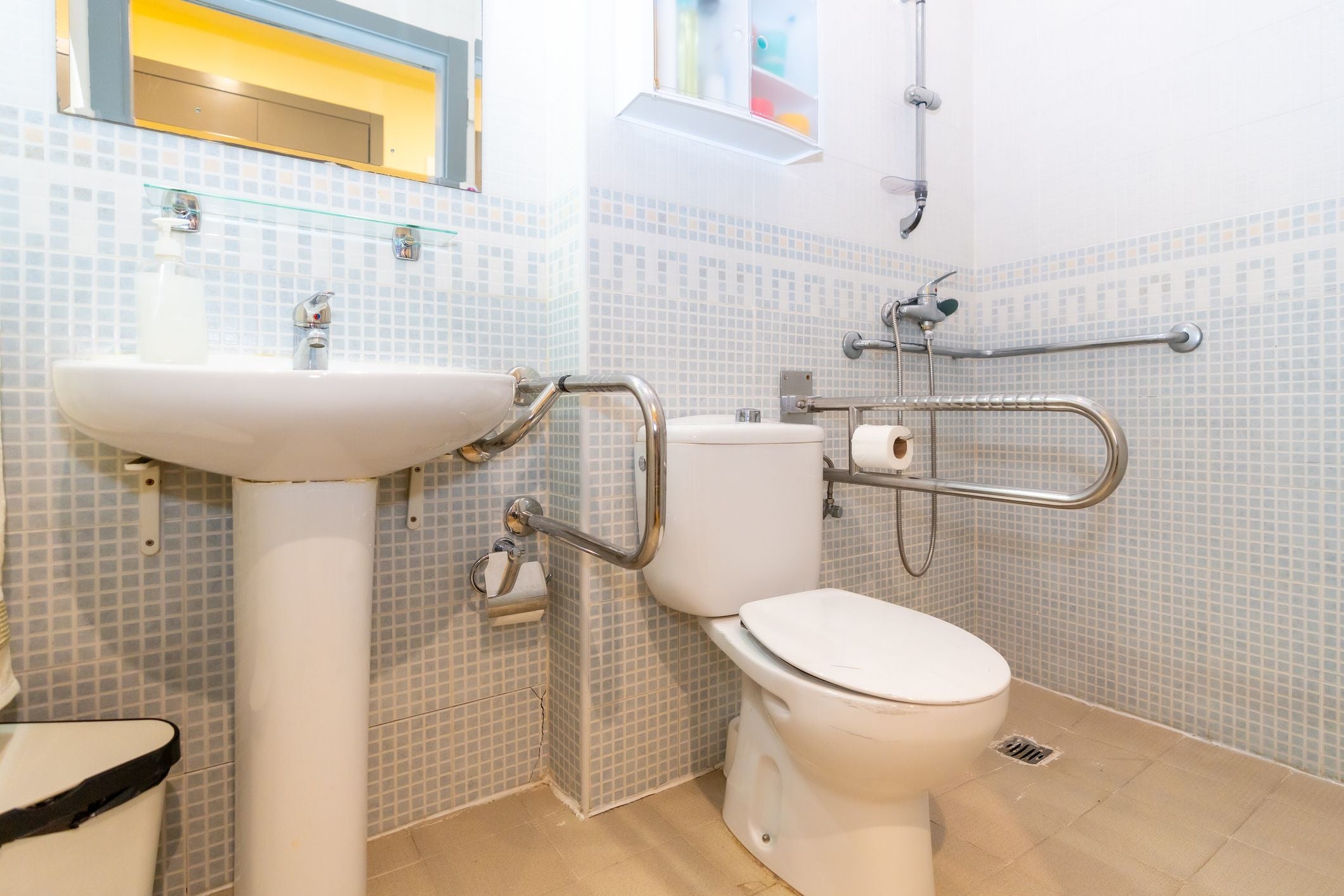 Barrierefreies Badezimmer mit Haltegriffen, Toilette, Waschbecken und Dusche in einer Geriatrie.