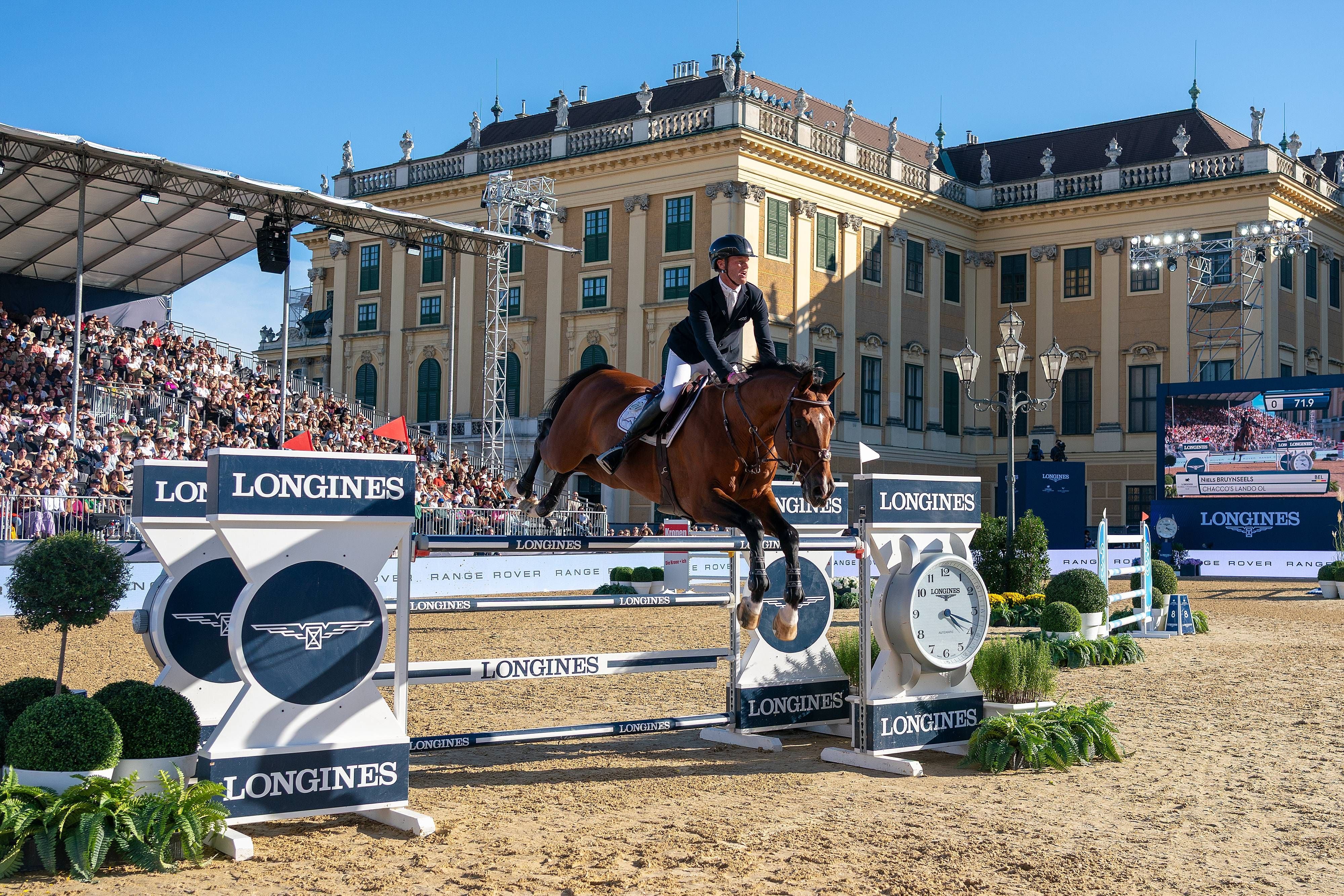 Springreiter springt mit Pferd über Hindernis beim Turnier vor Schloss Schönbrunn in Wien.