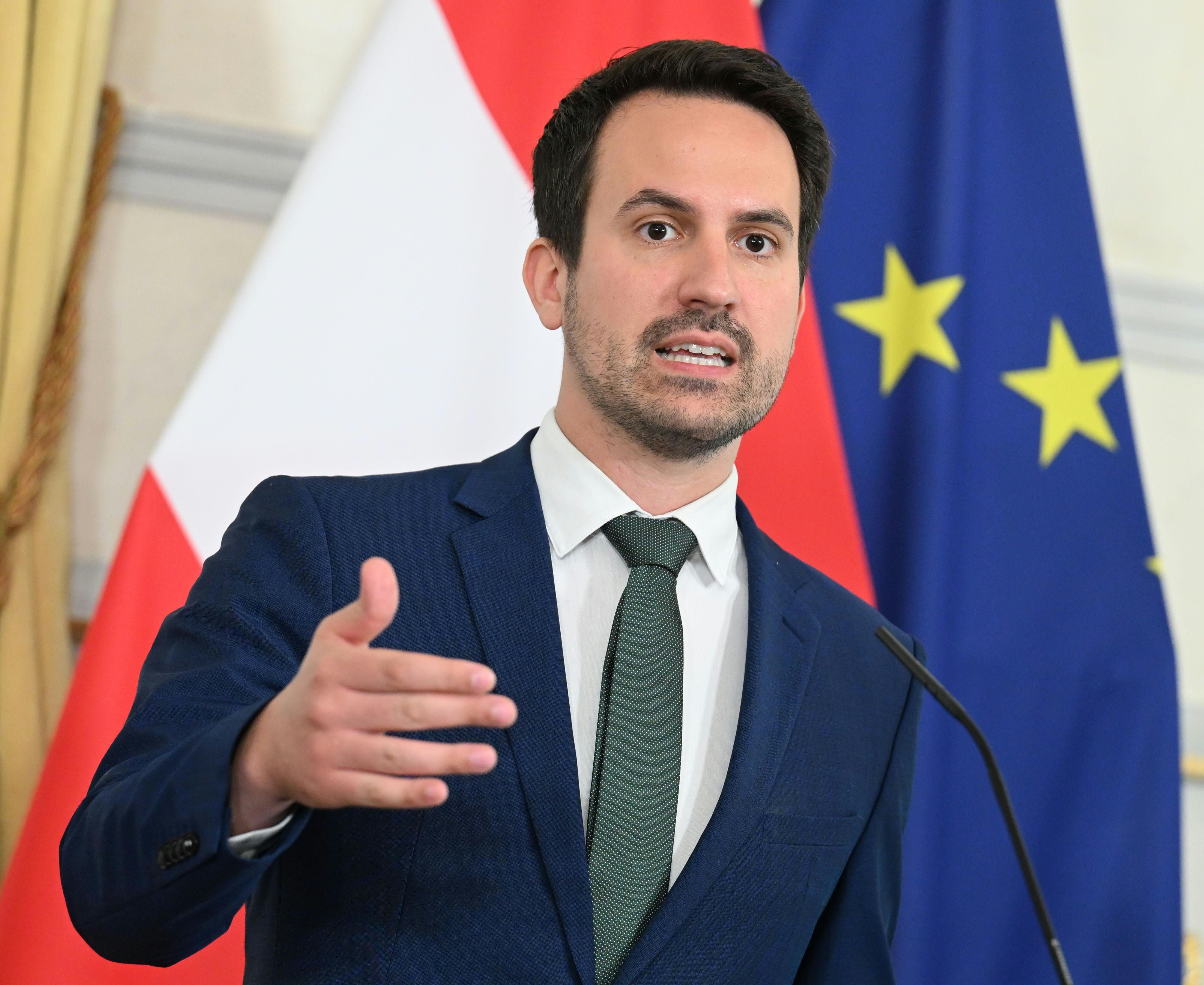 Ein Mann im Anzug spricht bei einer Pressekonferenz vor österreichischer und EU-Flagge.