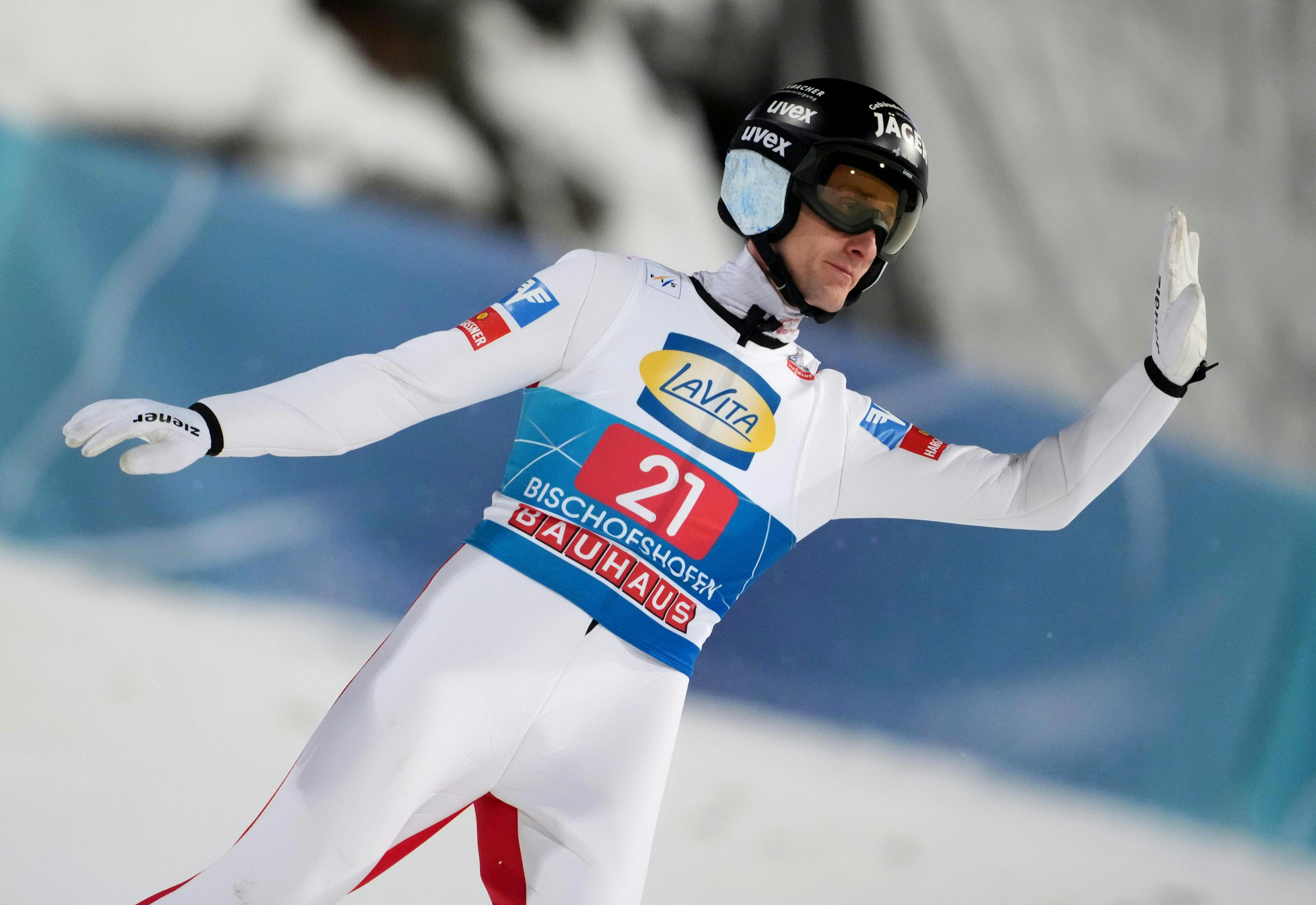 Skispringer in weißem Anzug und Helm bei der Landung auf einer Skisprungschanze.