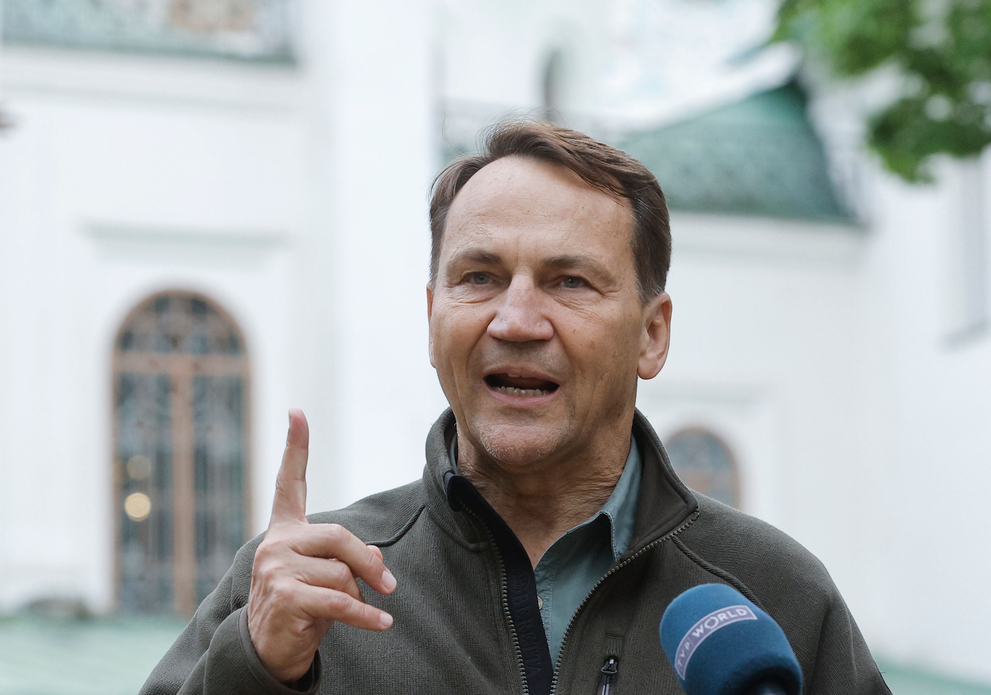 Ein Mann spricht bei einer Pressekonferenz und hebt einen Finger, ein Mikrofon ist vor ihm.