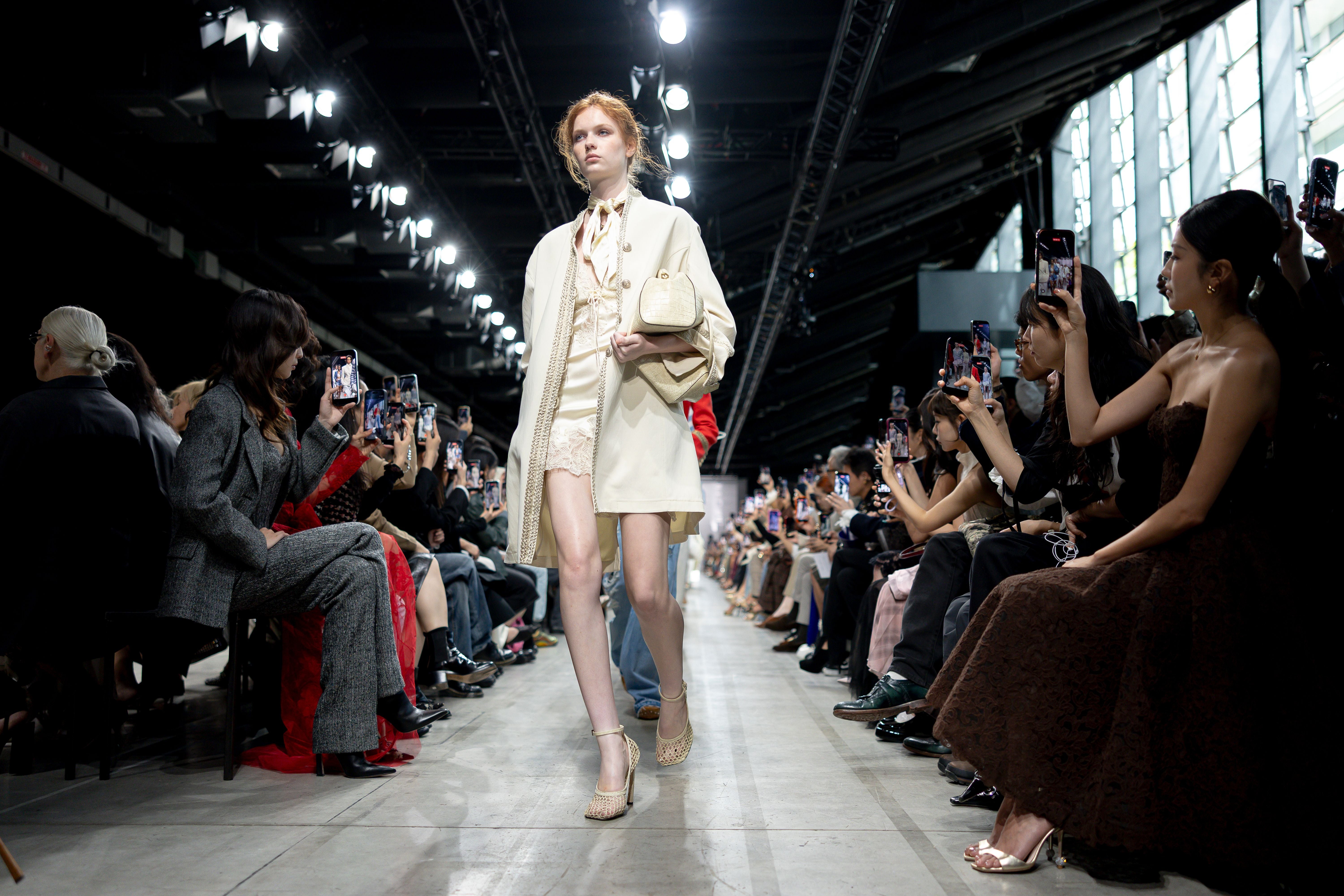 Model läuft auf der Modenschau-Runway, das Publikum fotografiert mit Smartphones.