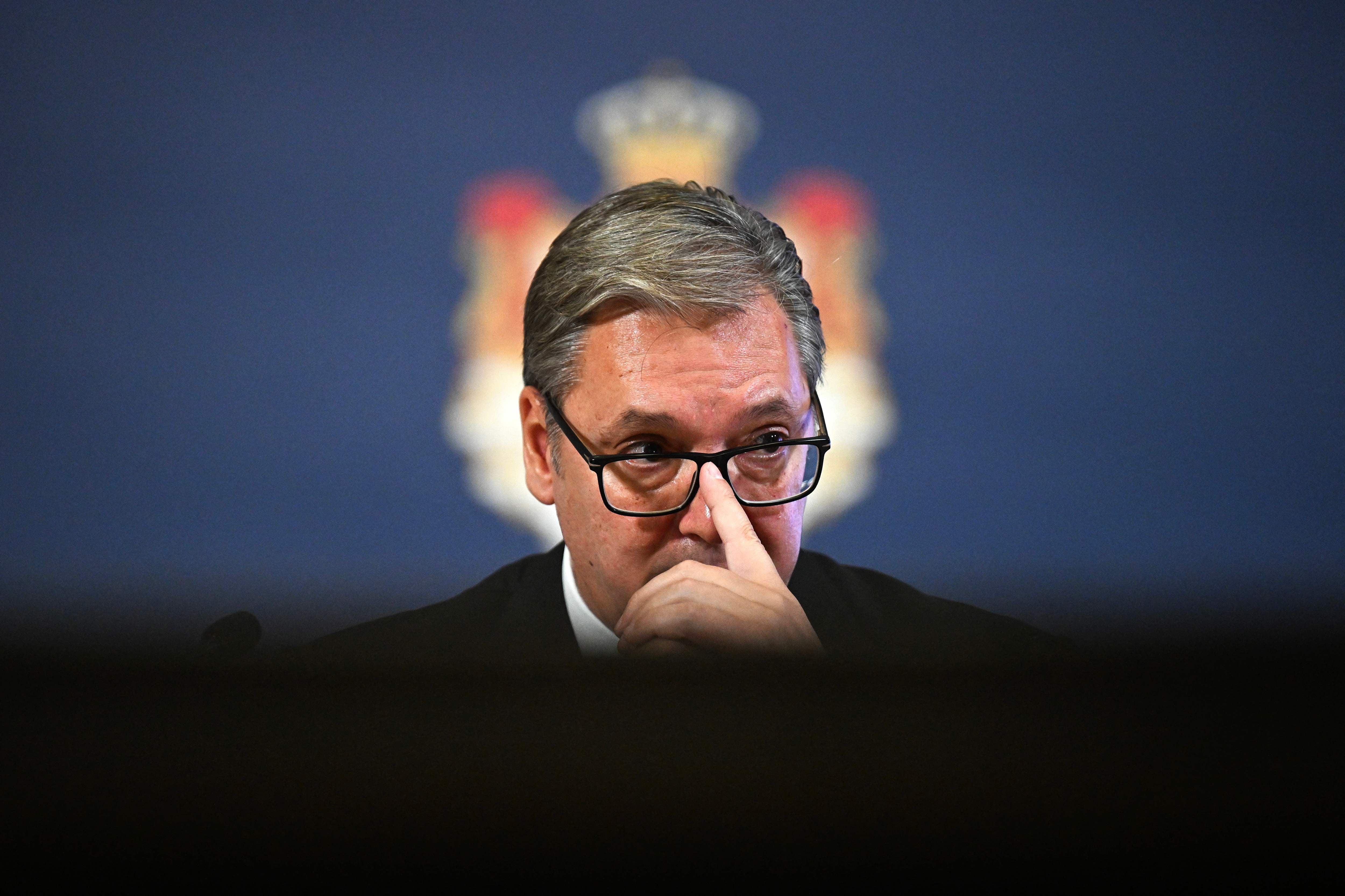 Ein Mann mit Brille spricht bei einer Pressekonferenz vor einem dunklen Hintergrund.