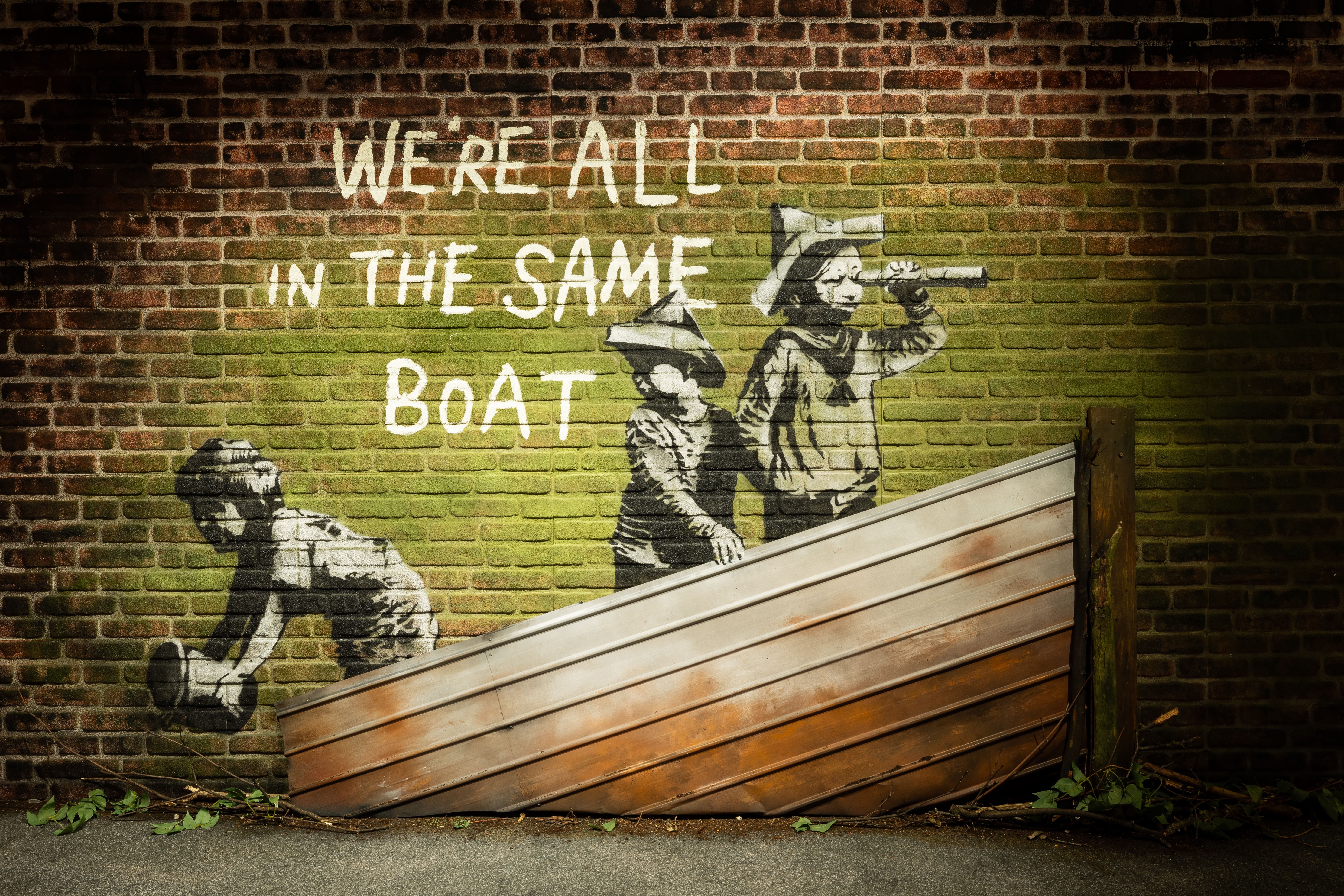 Banksy-Graffiti mit Kindern in einem halben Boot und dem Text "We're all in the same boat".