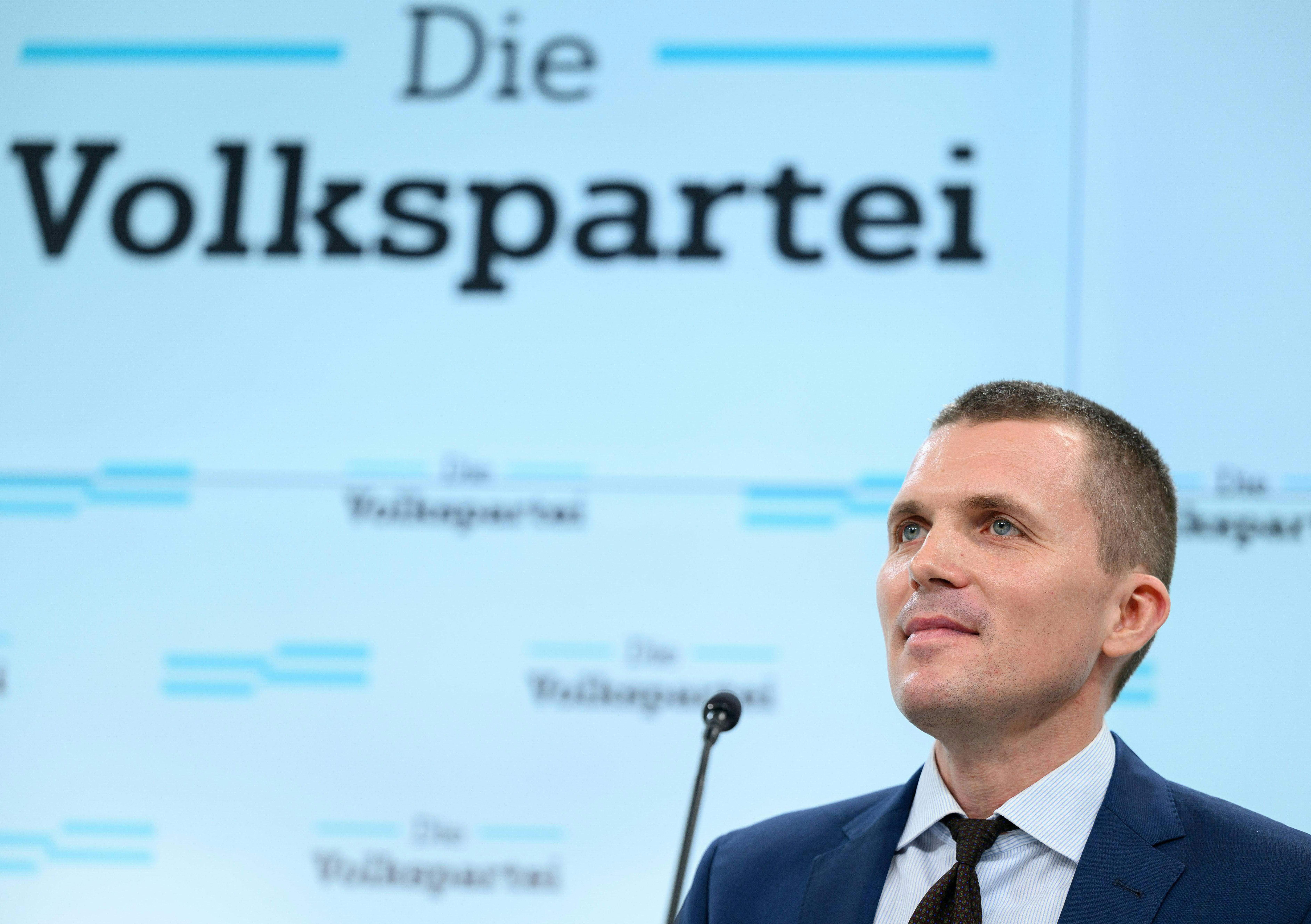 Ein Mann im Anzug steht vor einem Bildschirm mit der Aufschrift „Die Volkspartei“.