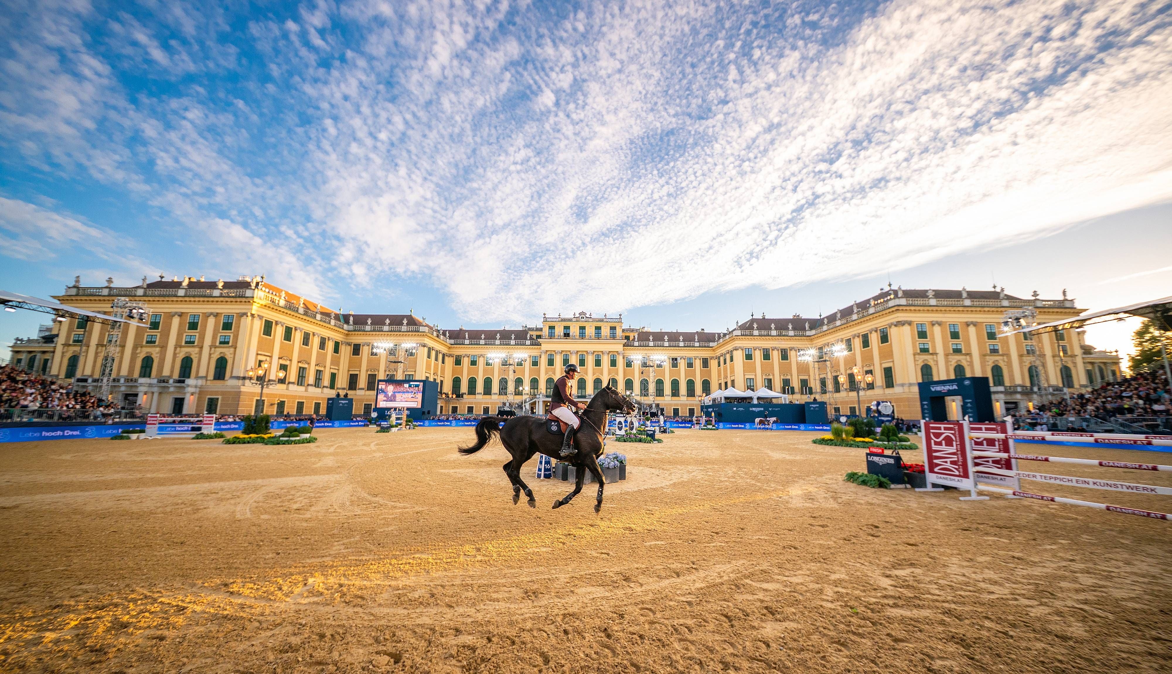 Springreiter mit Pferd beim Turnier vor Schloss Schönbrunn unter blauem Himmel in Wien.