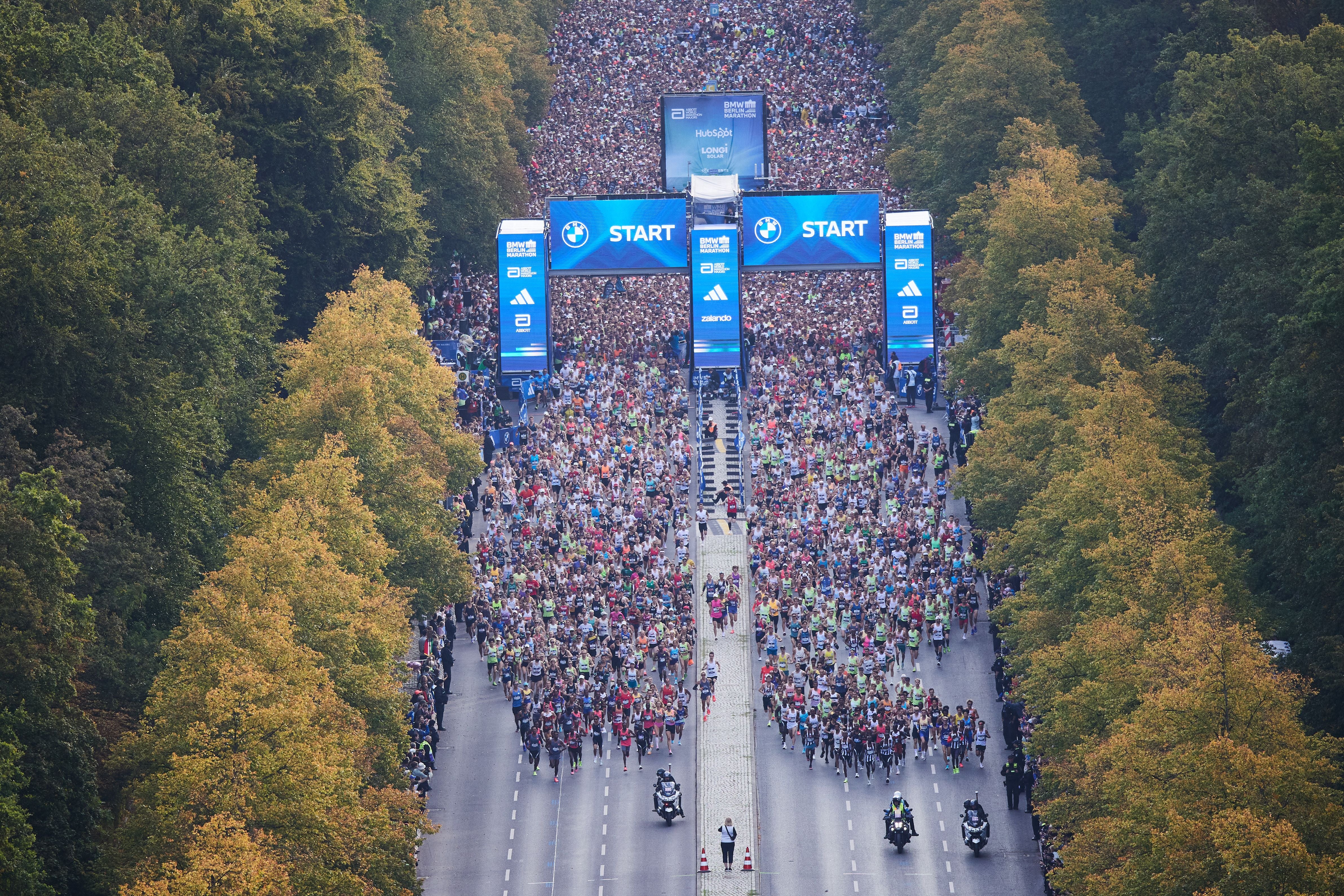 Tausende Läufer starten beim Berlin Marathon auf einer von Bäumen gesäumten Straße.