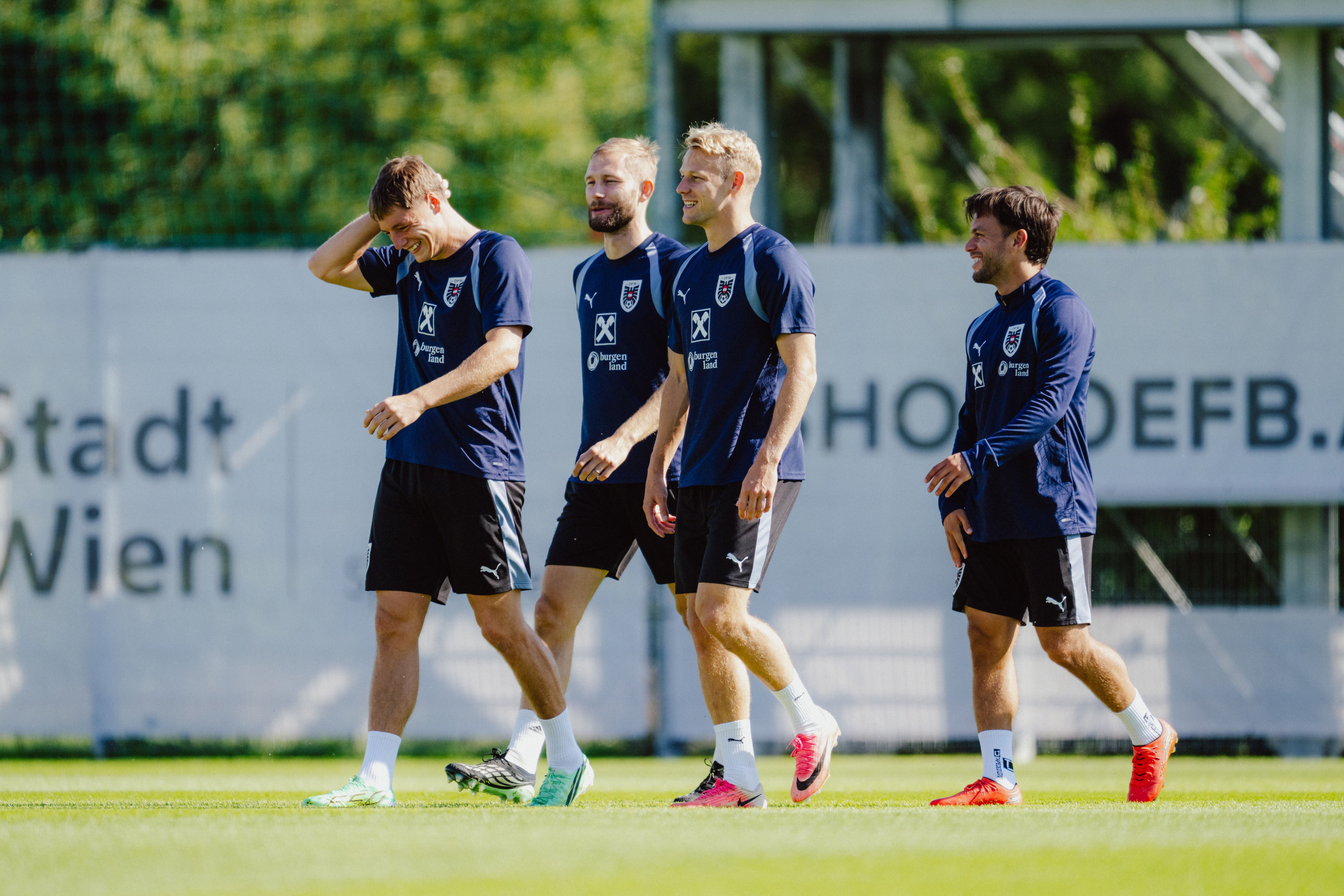 Vier österreichische Fußballspieler gehen lachend im Trainingsanzug über den Rasen.