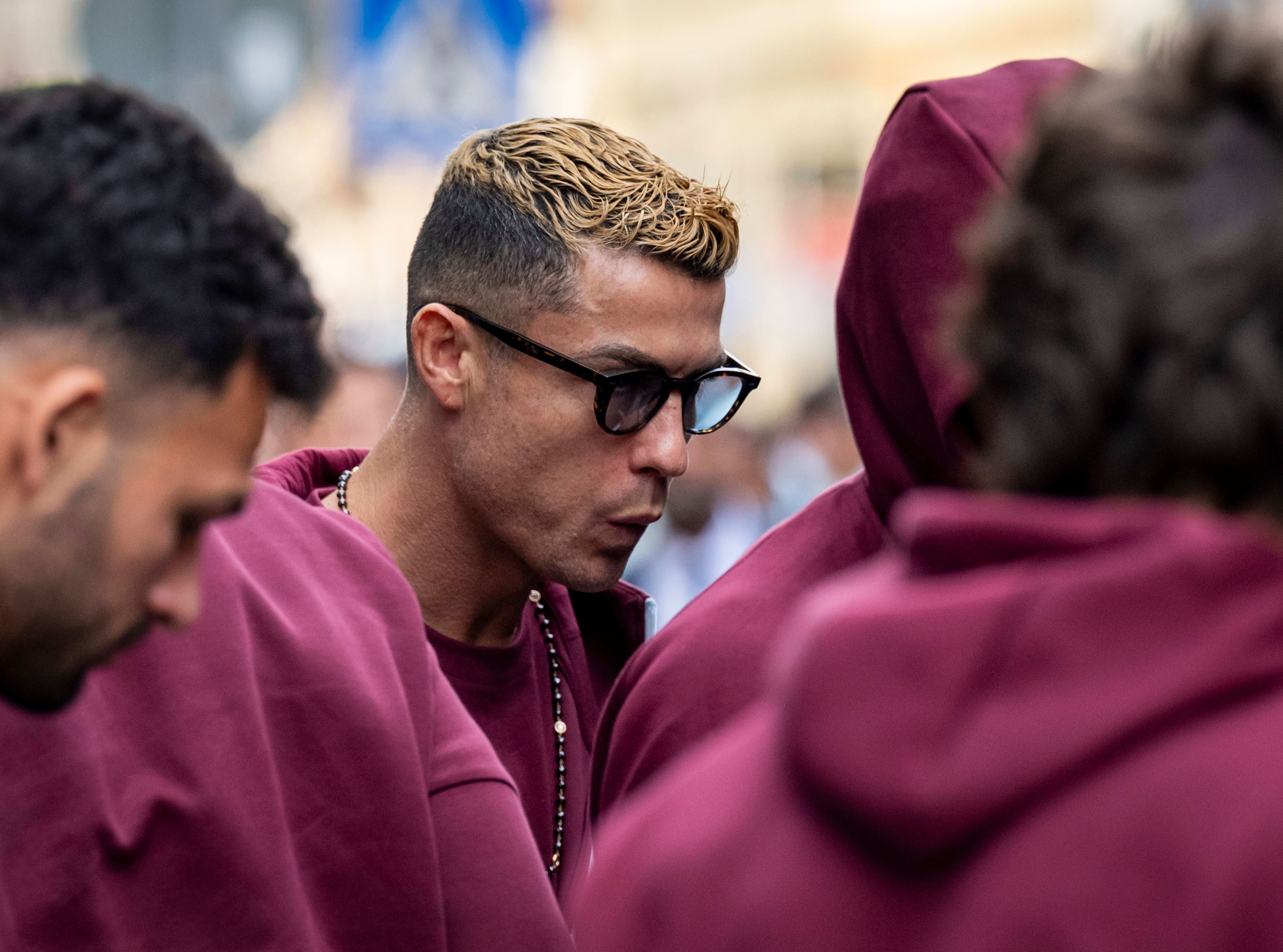 Mehrere Männer in bordeauxfarbenen Trainingsanzügen, einer trägt eine Sonnenbrille.