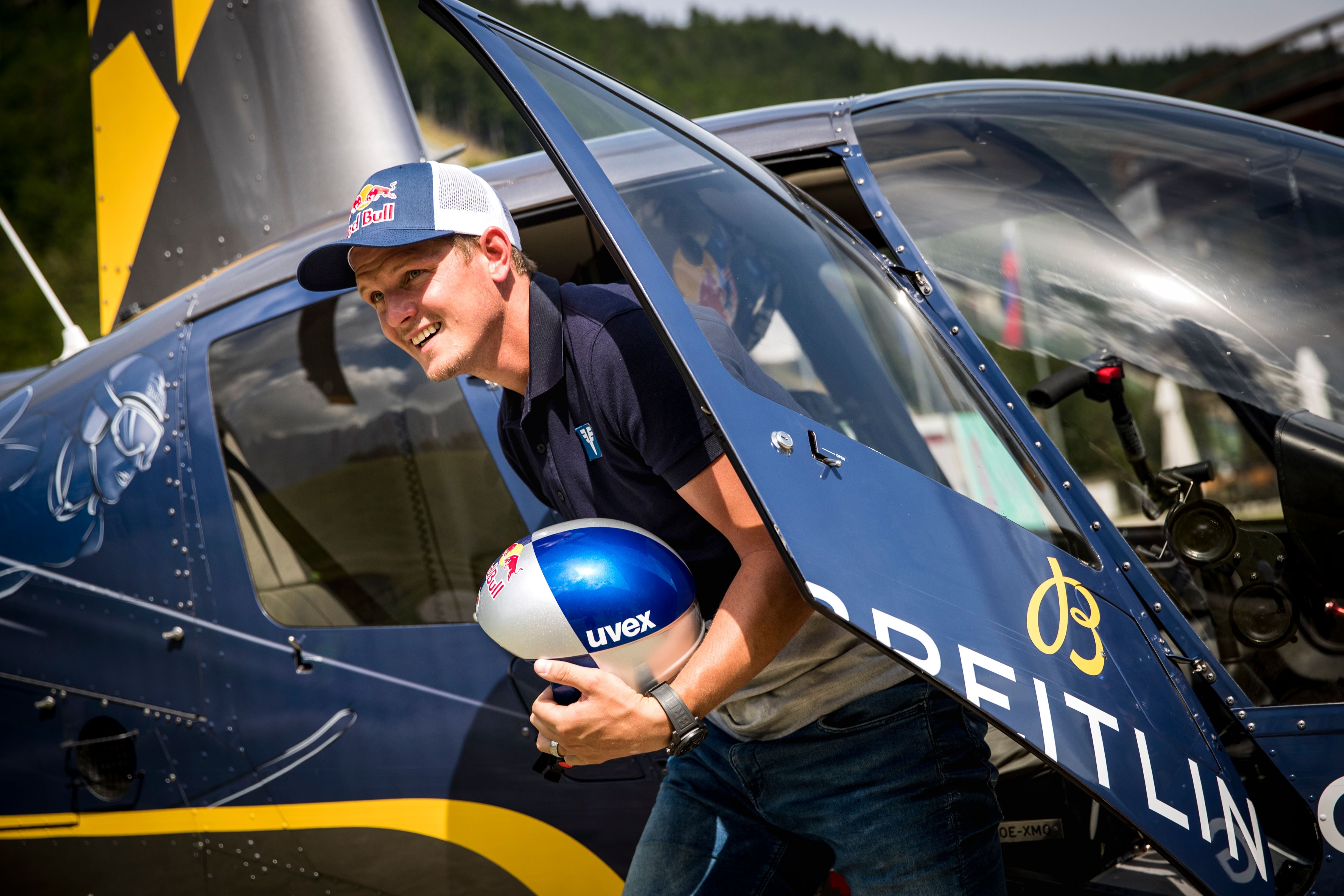 Ein Mann mit Basecap steigt mit Helm aus einem blauen Helikopter aus.