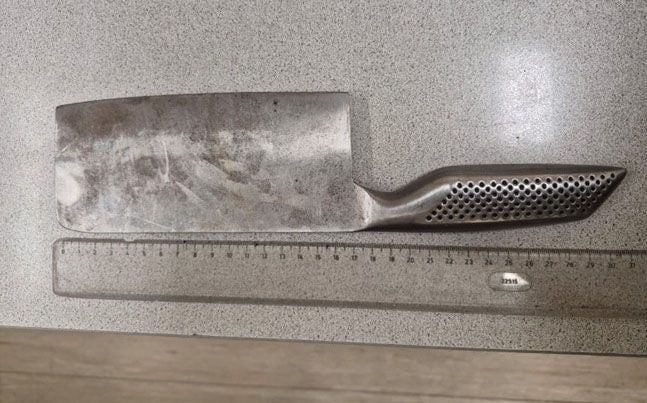 Ein Metallbeil mit Lochgriff liegt neben einem 30-cm-Lineal auf einer grauen Oberfläche.