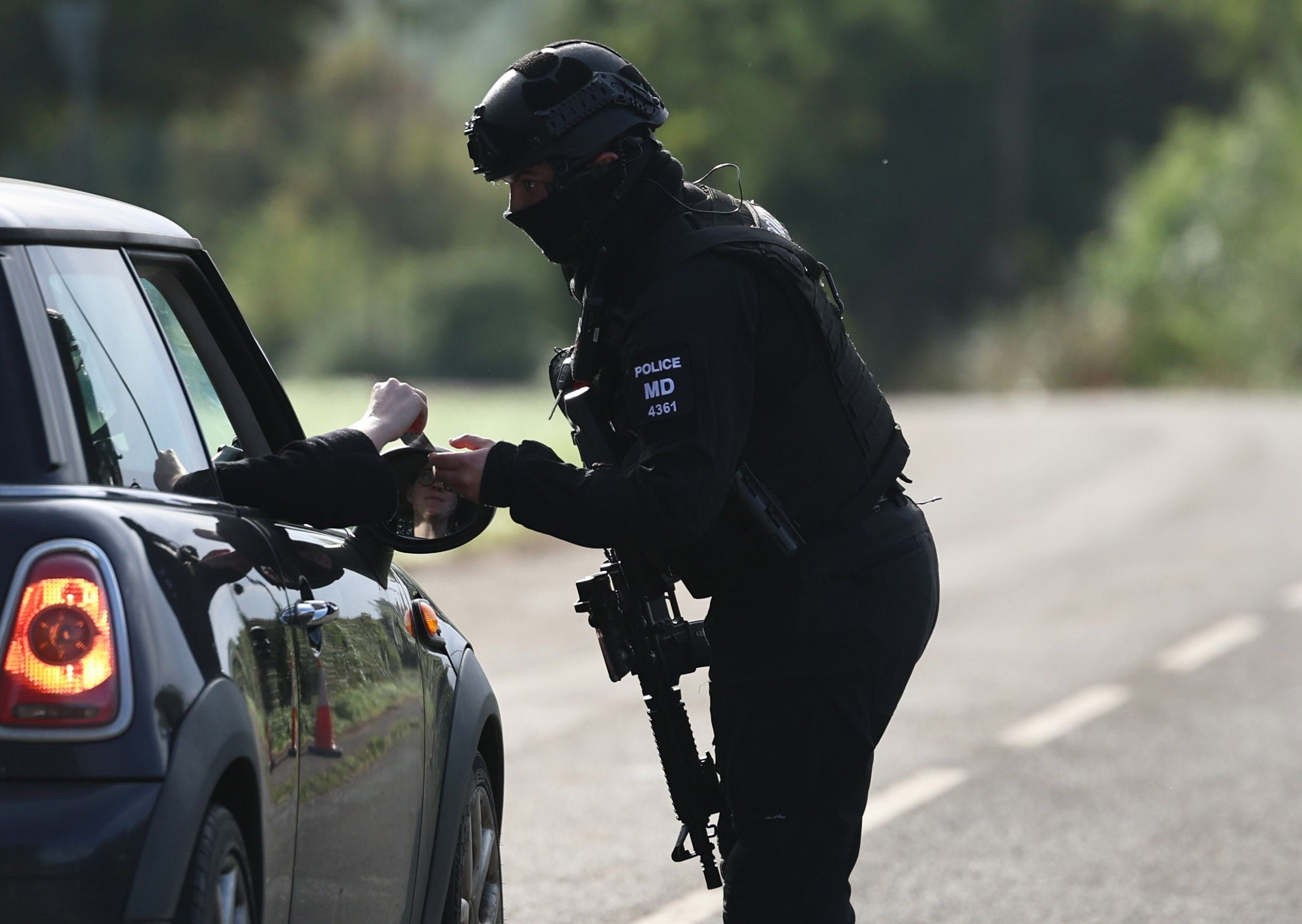 Ein bewaffneter Polizist kontrolliert die Ausweise eines Autofahrers an einer Straßensperre.
