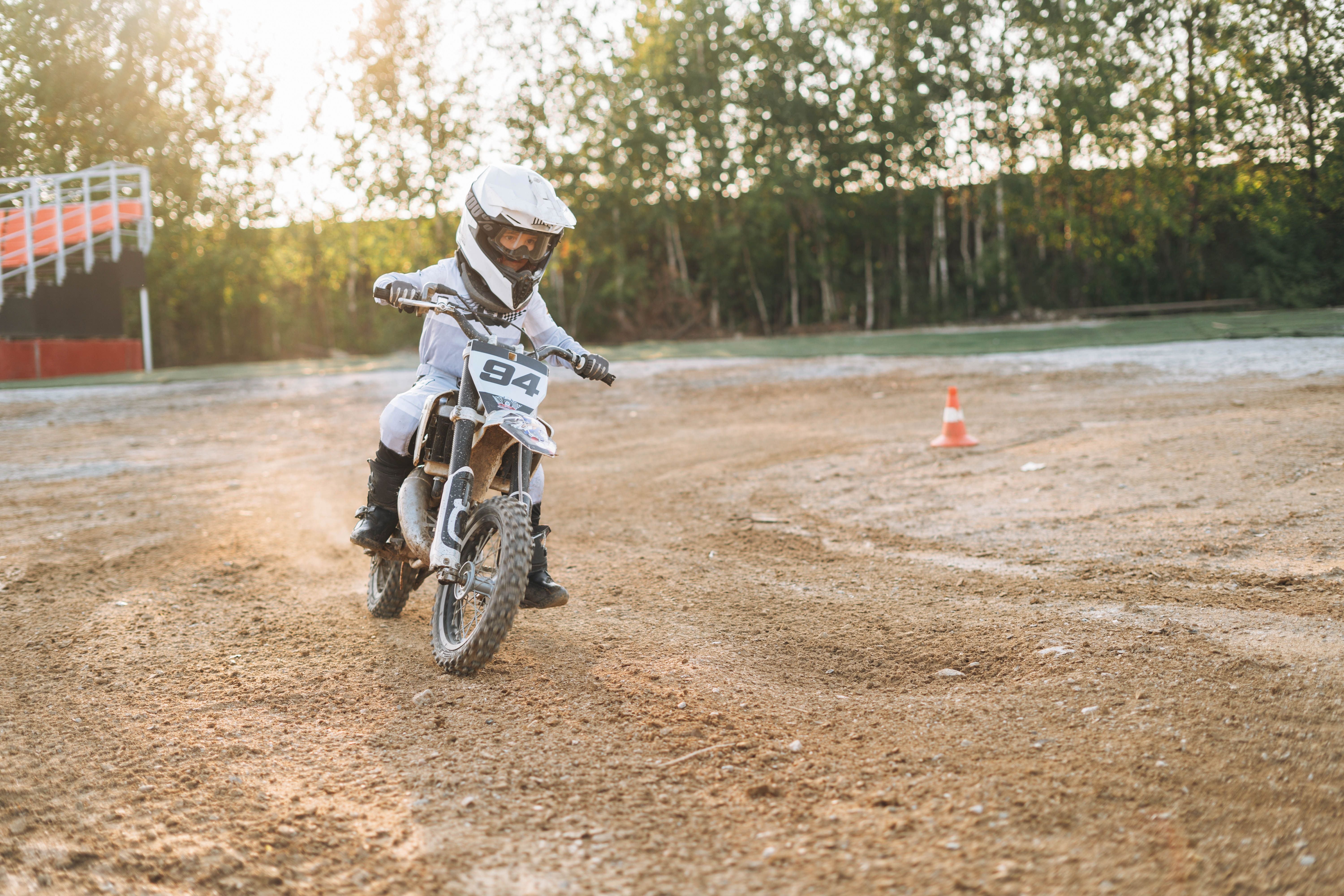 Junge mit Schutzkleidung fährt auf einem Motocross-Bike über eine sandige Piste.