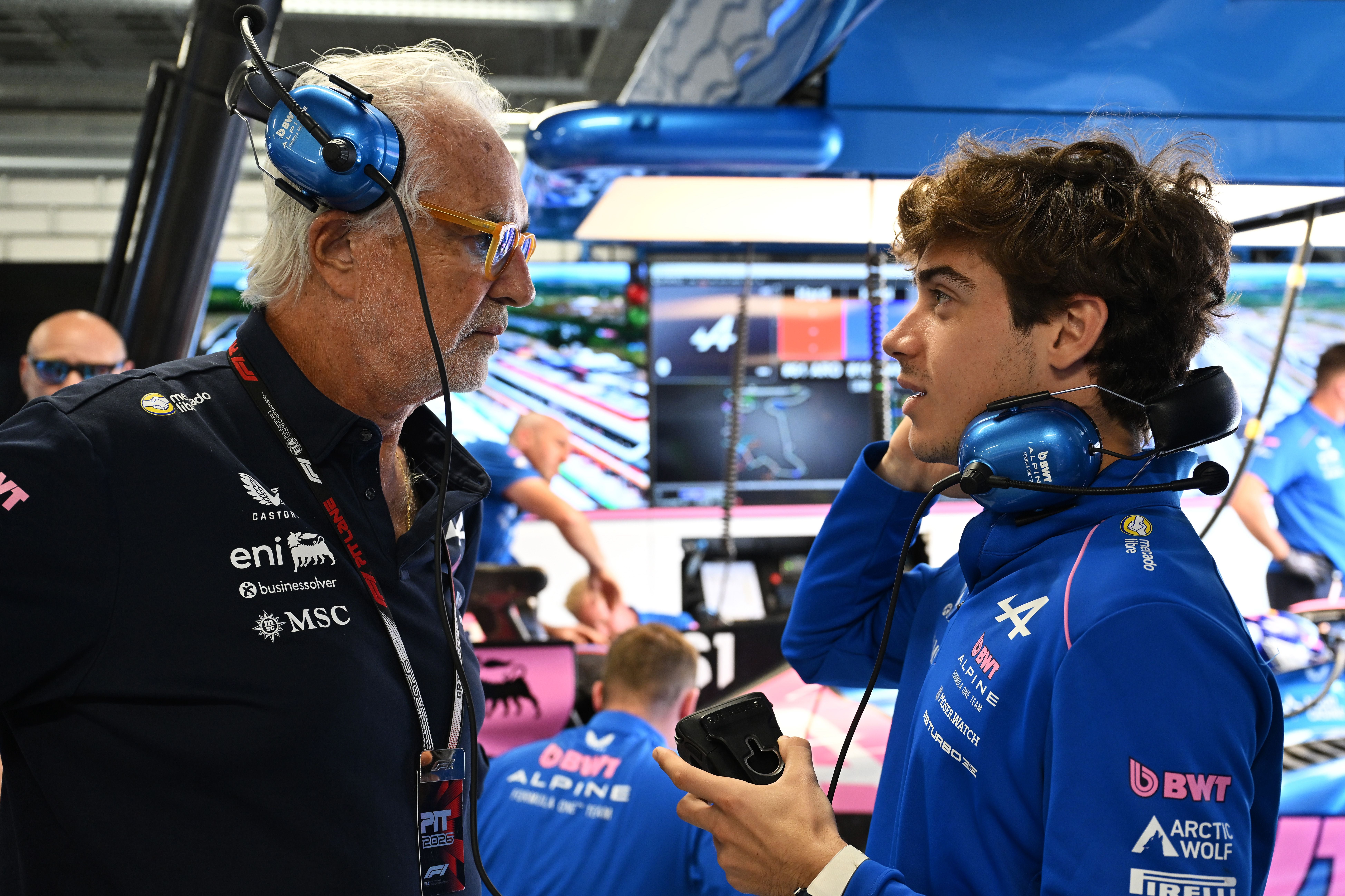 Zwei Männer mit Headsets unterhalten sich in der Alpine F1 Garage vor Bildschirmen und Technik.