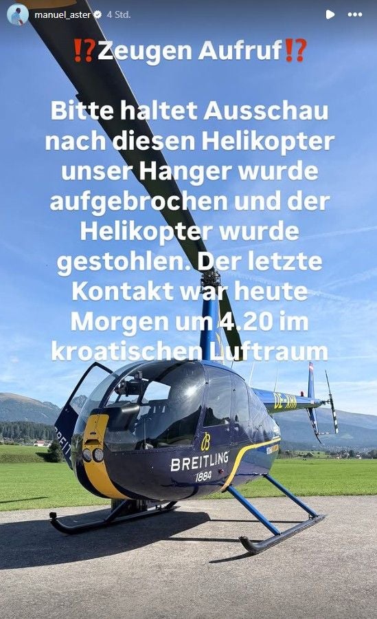 Ein blauer Robinson R44 Helikopter mit gelber „Breitling“-Beschriftung steht auf einer Wiese.