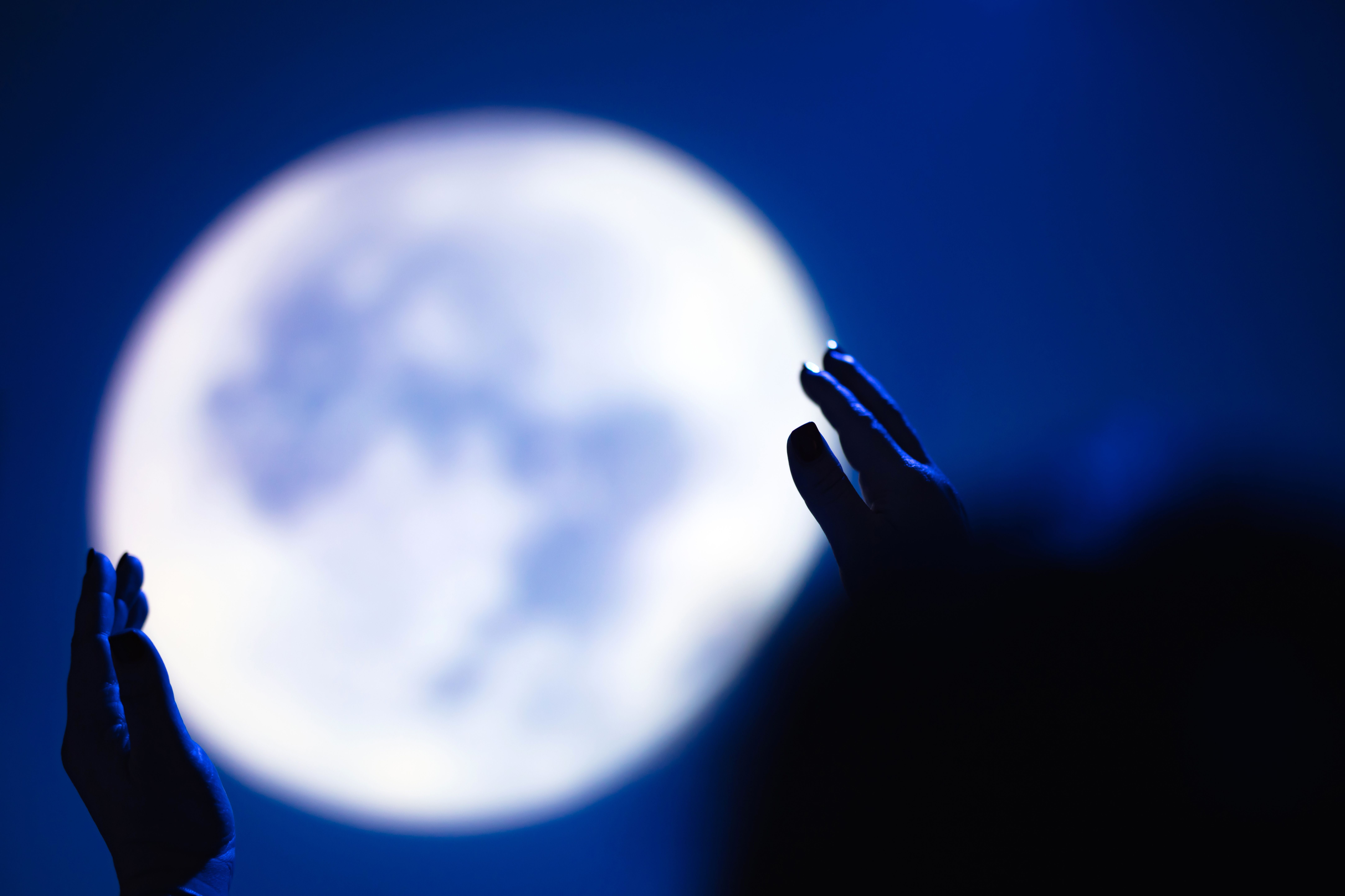 Zwei Hände sind vor einem großen, verschwommenen Vollmond am Nachthimmel zu sehen.