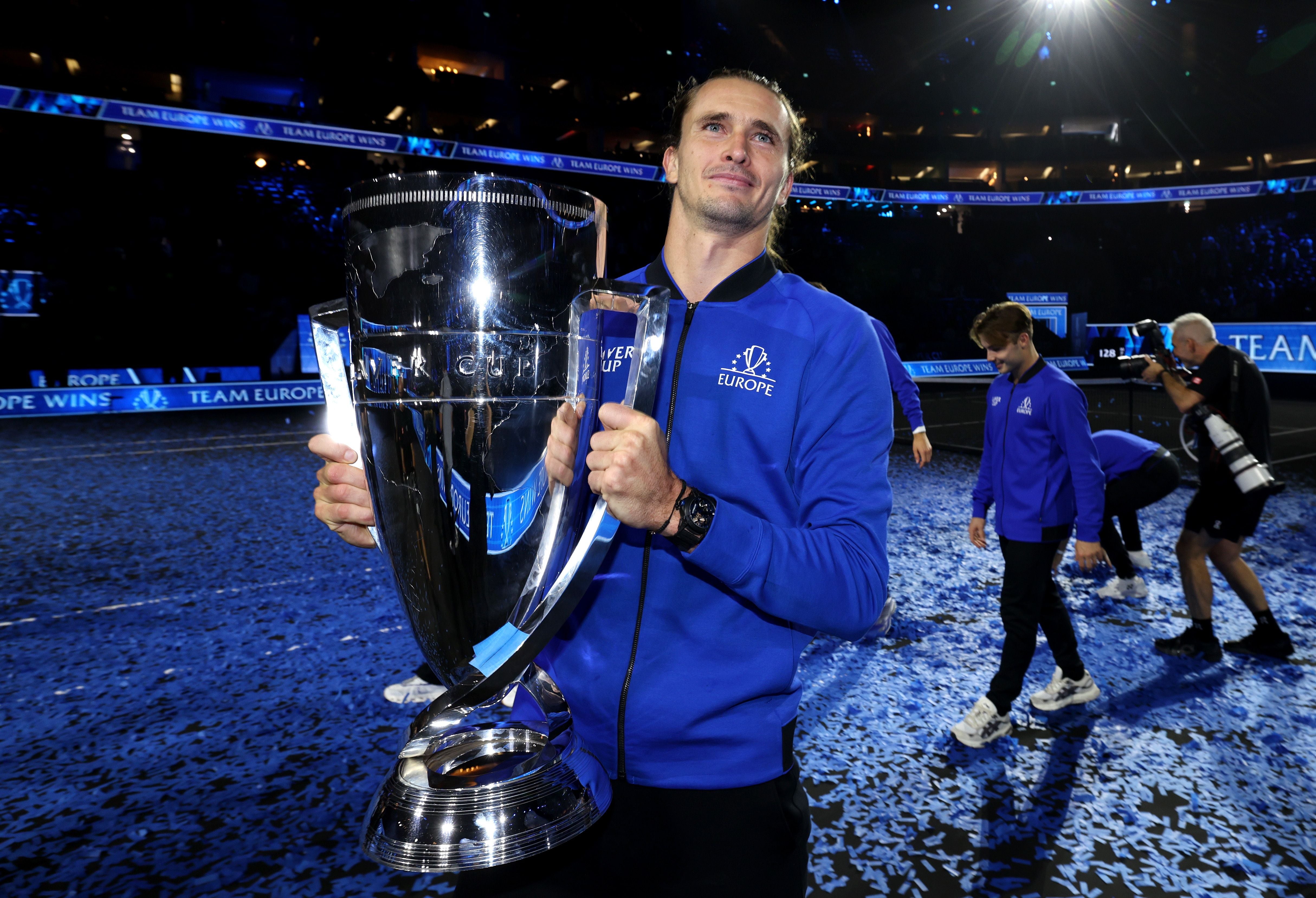 Ein Tennisspieler hält den Laver Cup-Pokal und feiert in einer Arena mit blauem Konfetti.