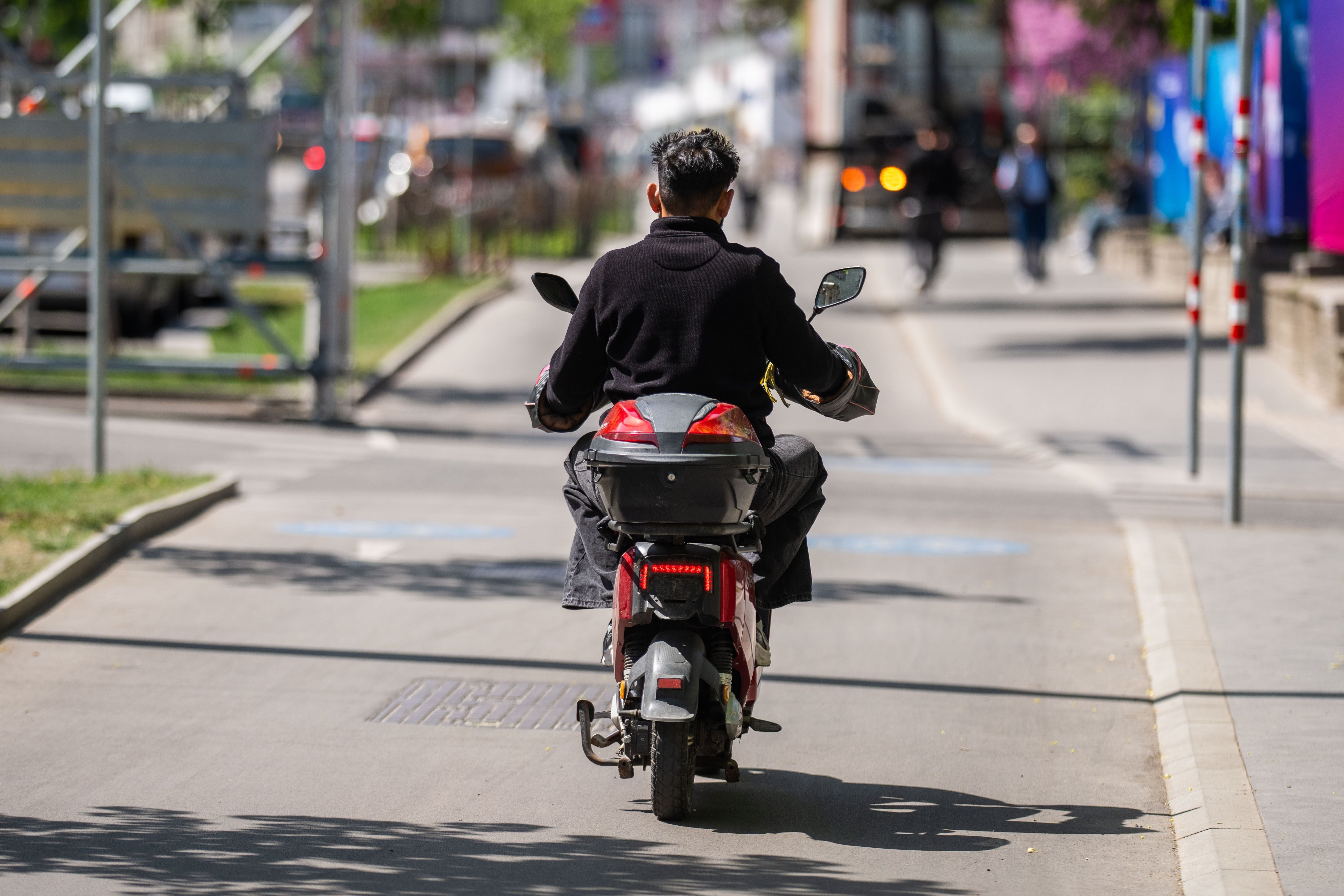 Ein E-Moped-Fahrer fährt auf einem Radweg in Wien bei sonnigem Wetter.