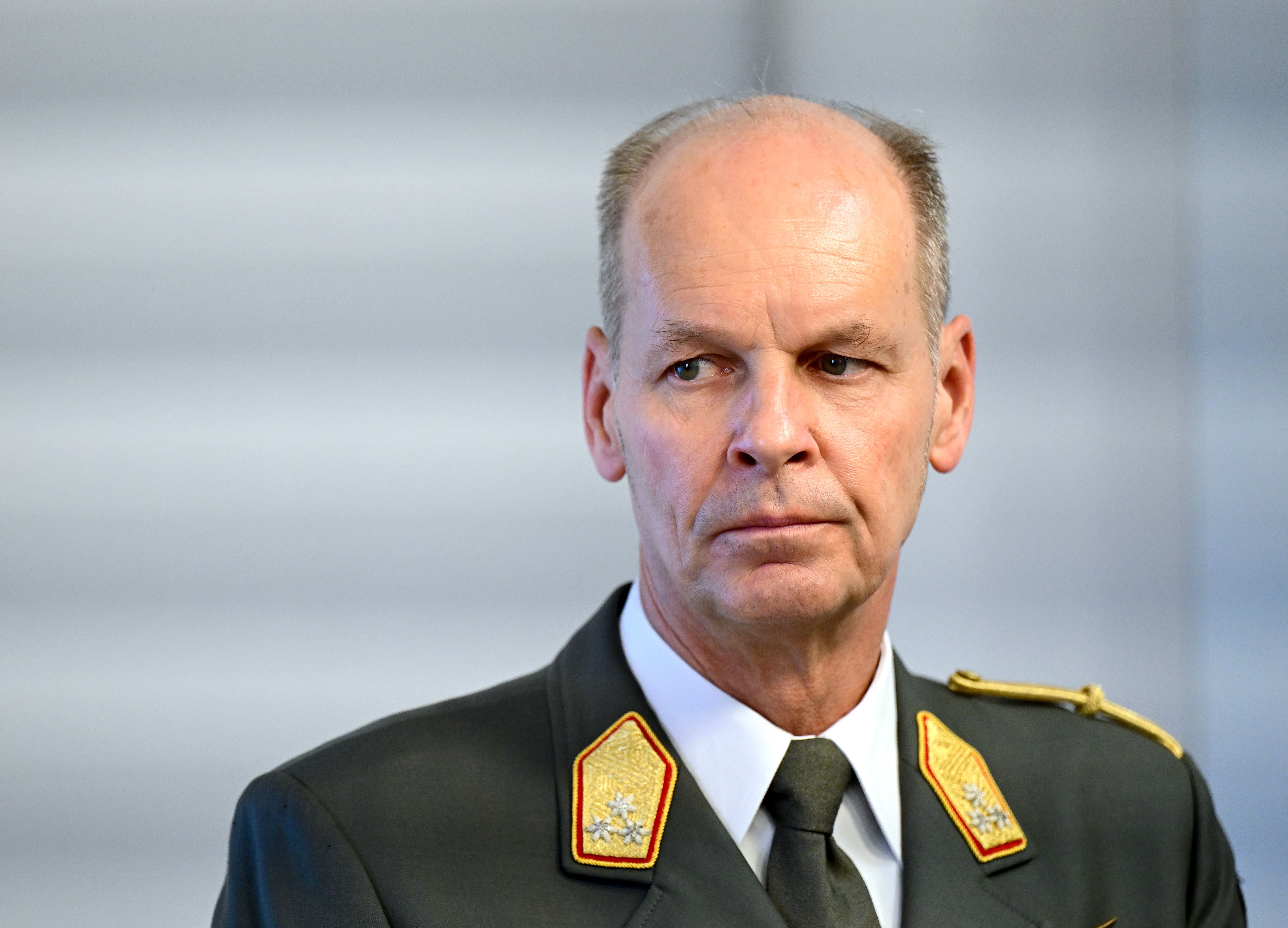 Ein Mann in Militäruniform mit goldenen Schulterabzeichen steht vor einem neutralen Hintergrund.