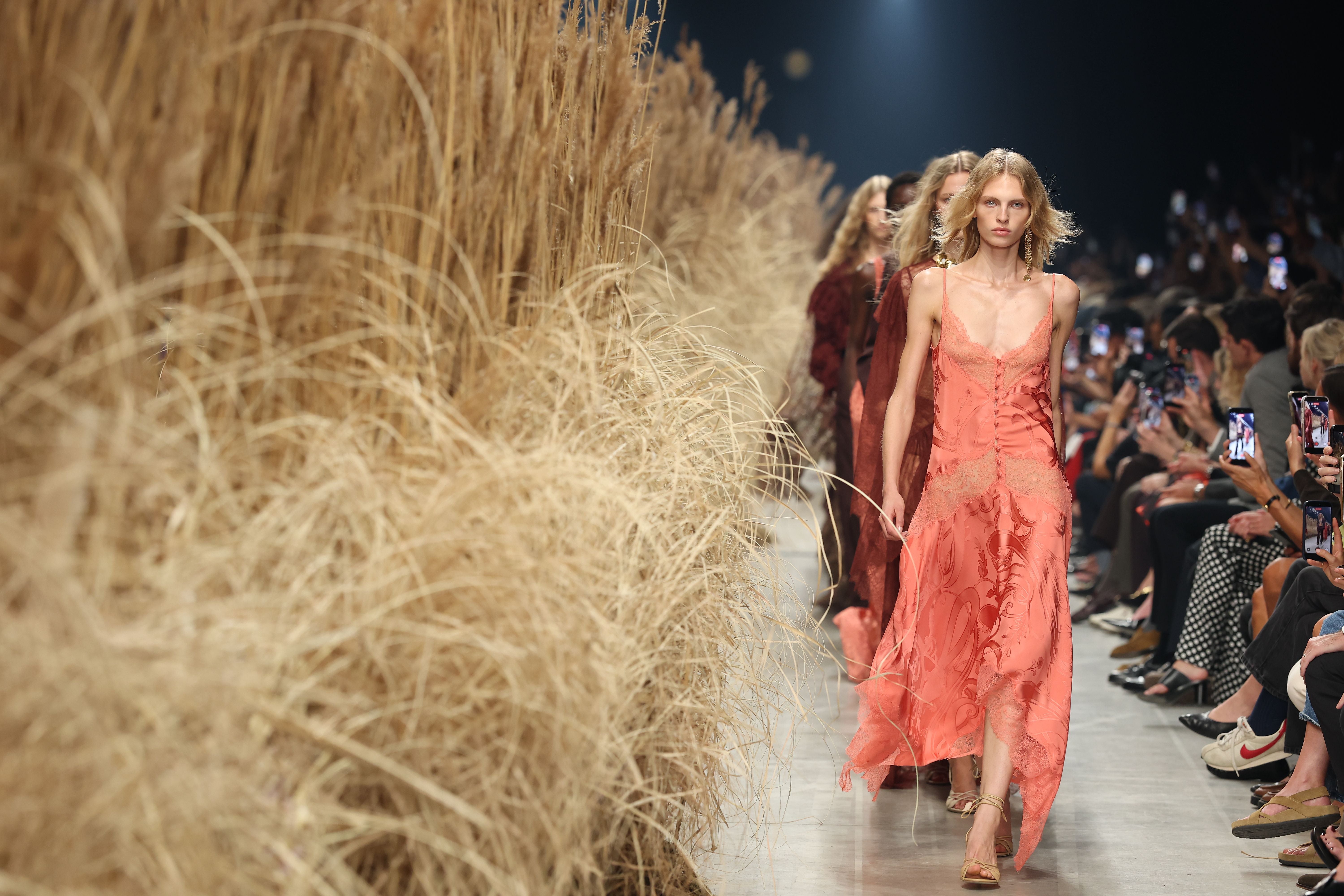 Models laufen bei einer Modenschau in Mailand an trockenen Gräsern vorbei auf dem Laufsteg.