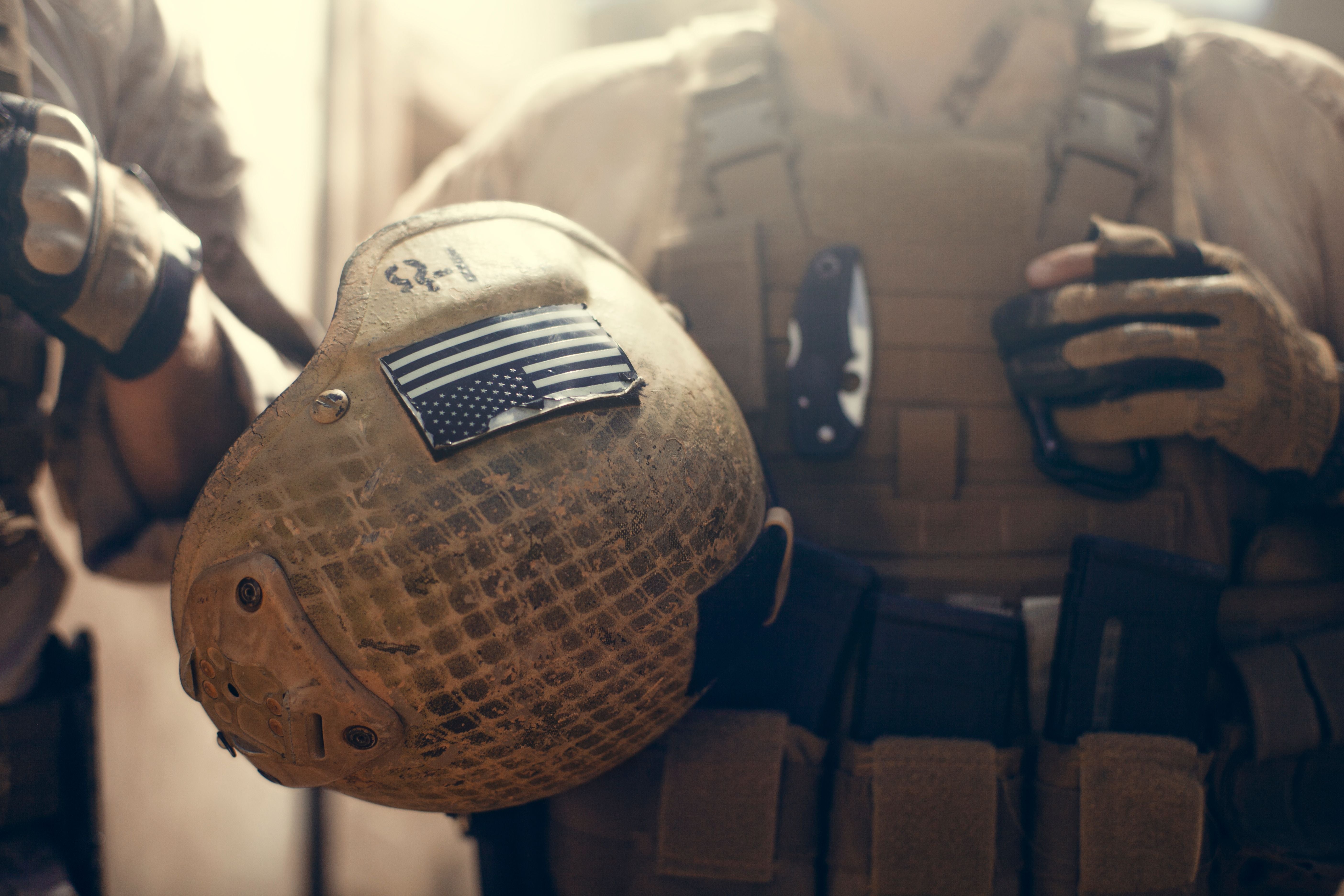US-Soldat hält Helm mit amerikanischer Flagge und taktischer Ausrüstung.